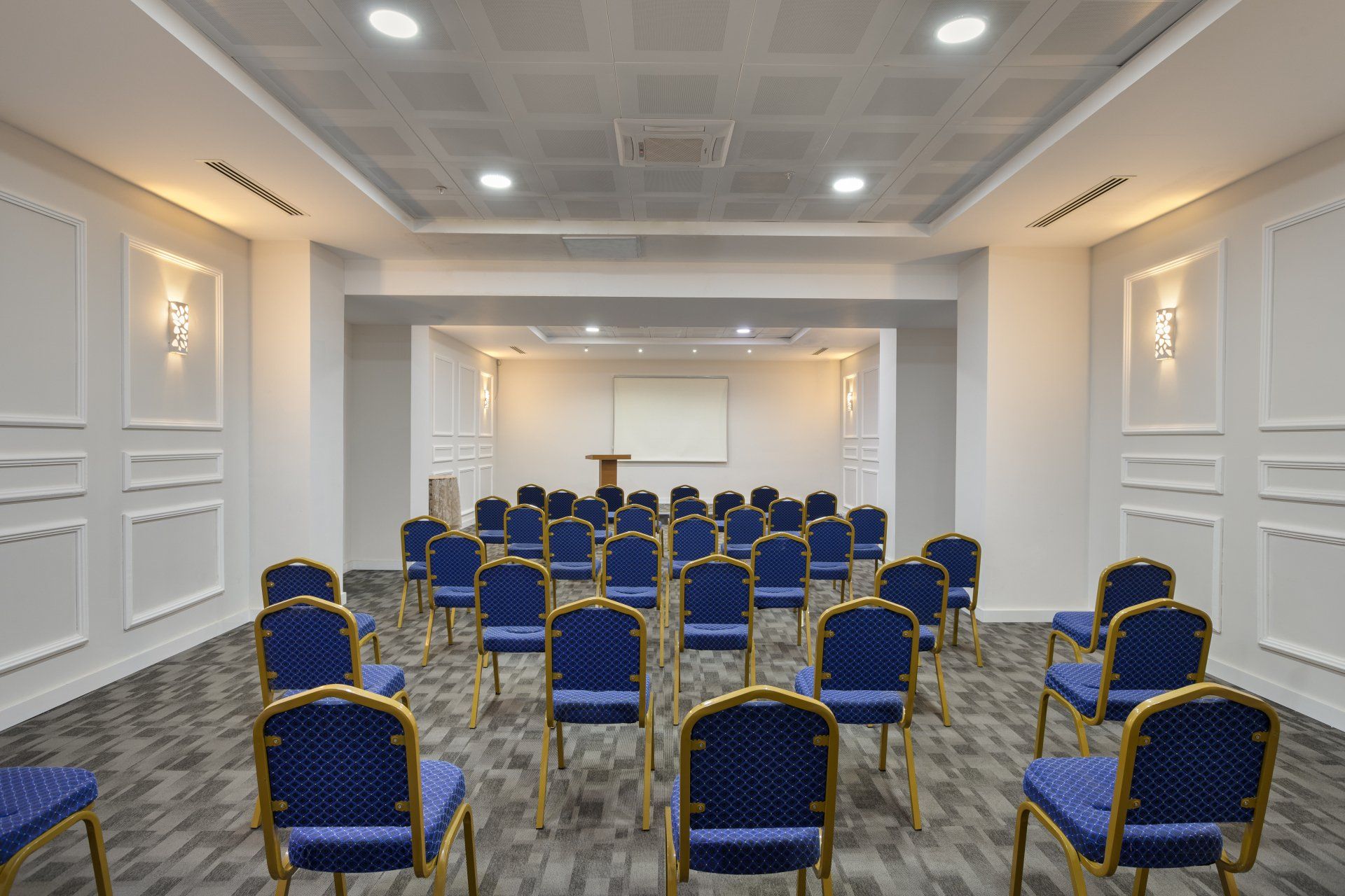 قاعة اجتماعات مليئة بالكراسي الزرقاء وشاشة كبيرة.