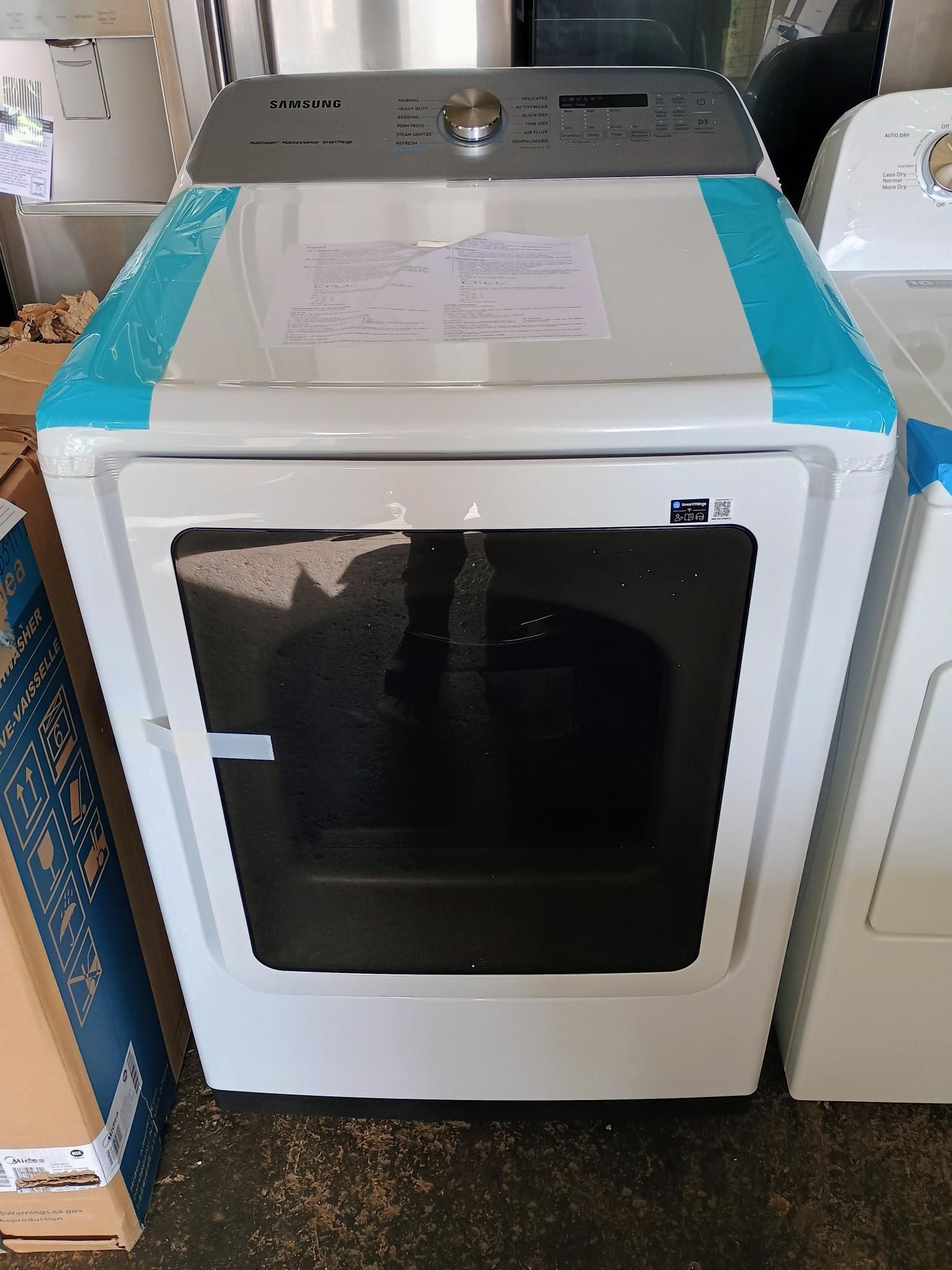 A white dryer is sitting on the floor next to a washer and dryer.