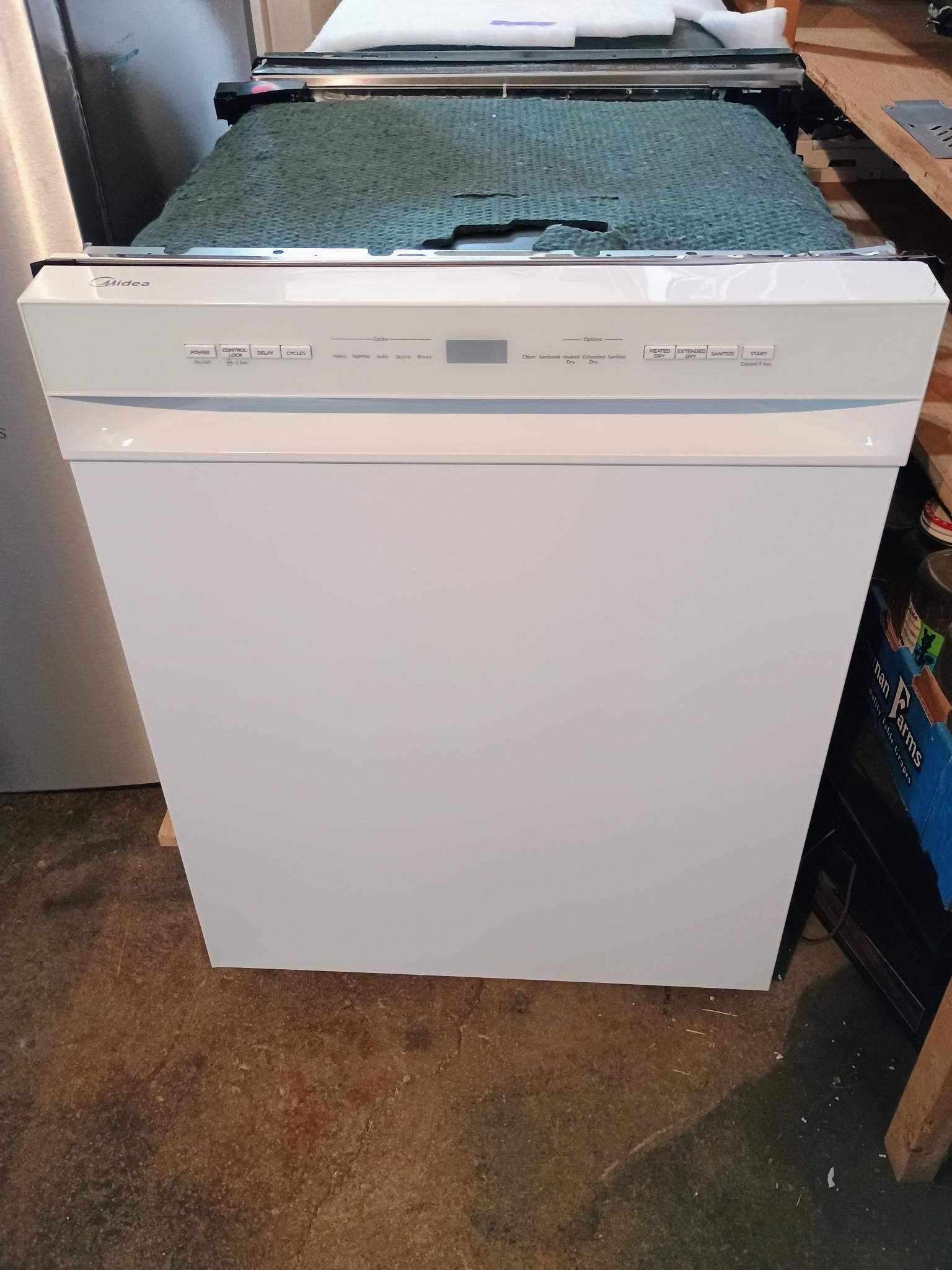 A white dishwasher is sitting on the floor in a kitchen.