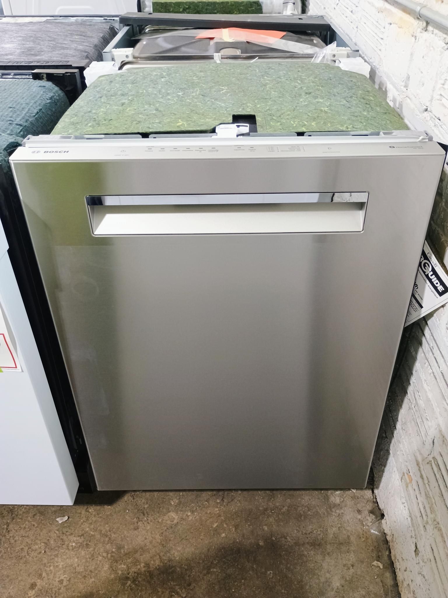 A stainless steel dishwasher is sitting on the floor next to a brick wall.