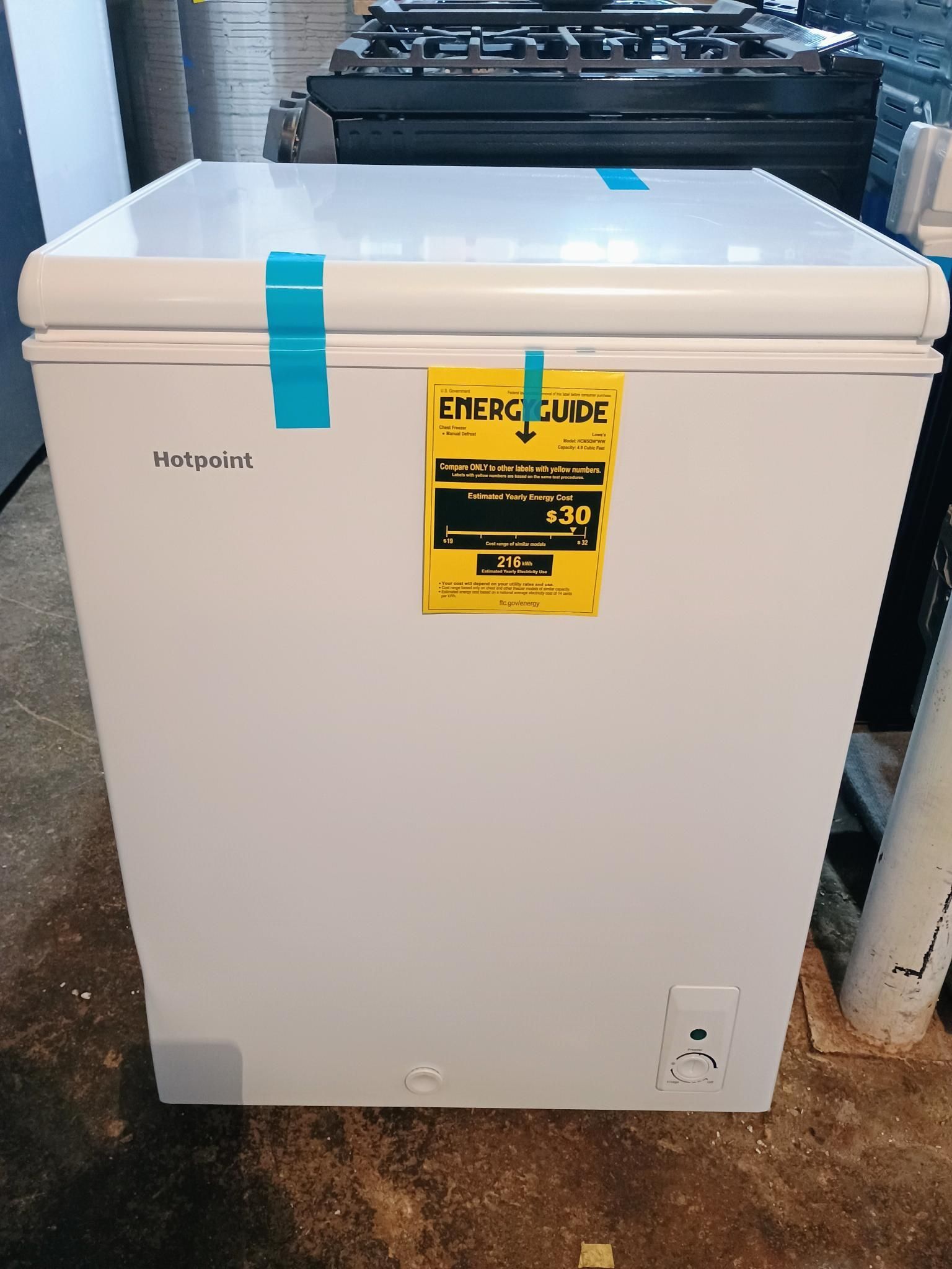 A white chest freezer is sitting on the floor next to a stove.