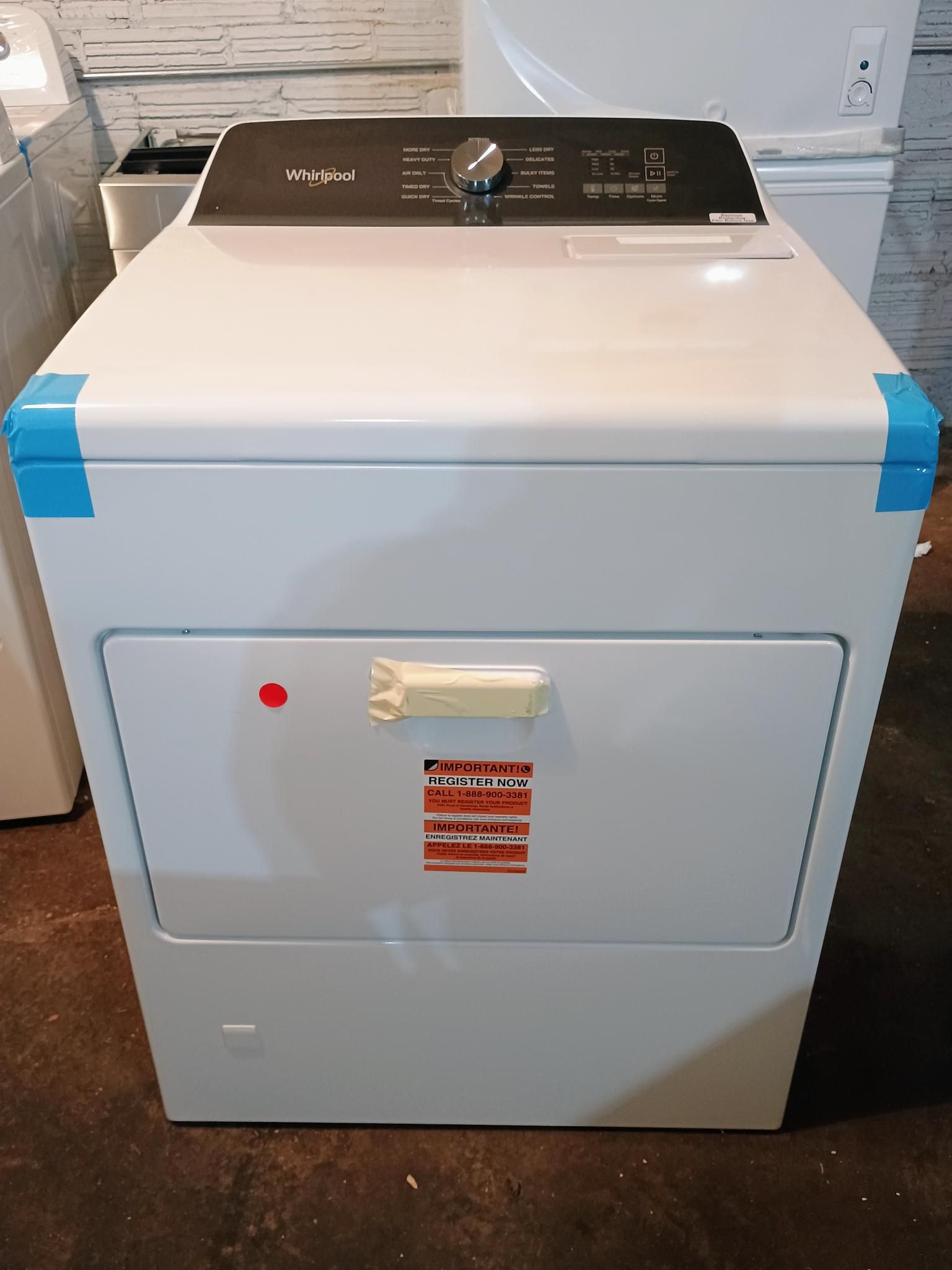 A white dryer is sitting on a wooden floor.