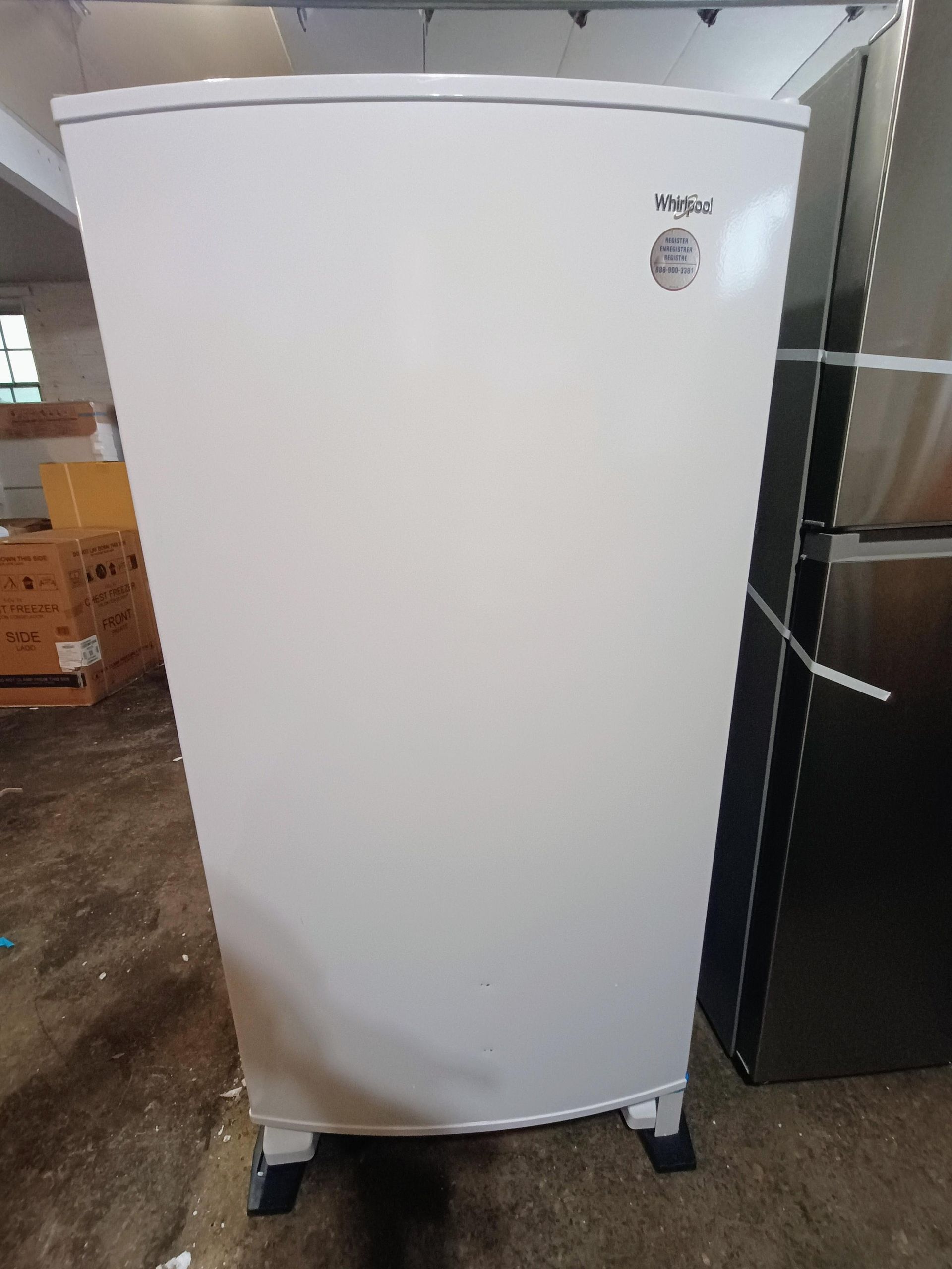 A white refrigerator is sitting in a warehouse next to a black refrigerator.