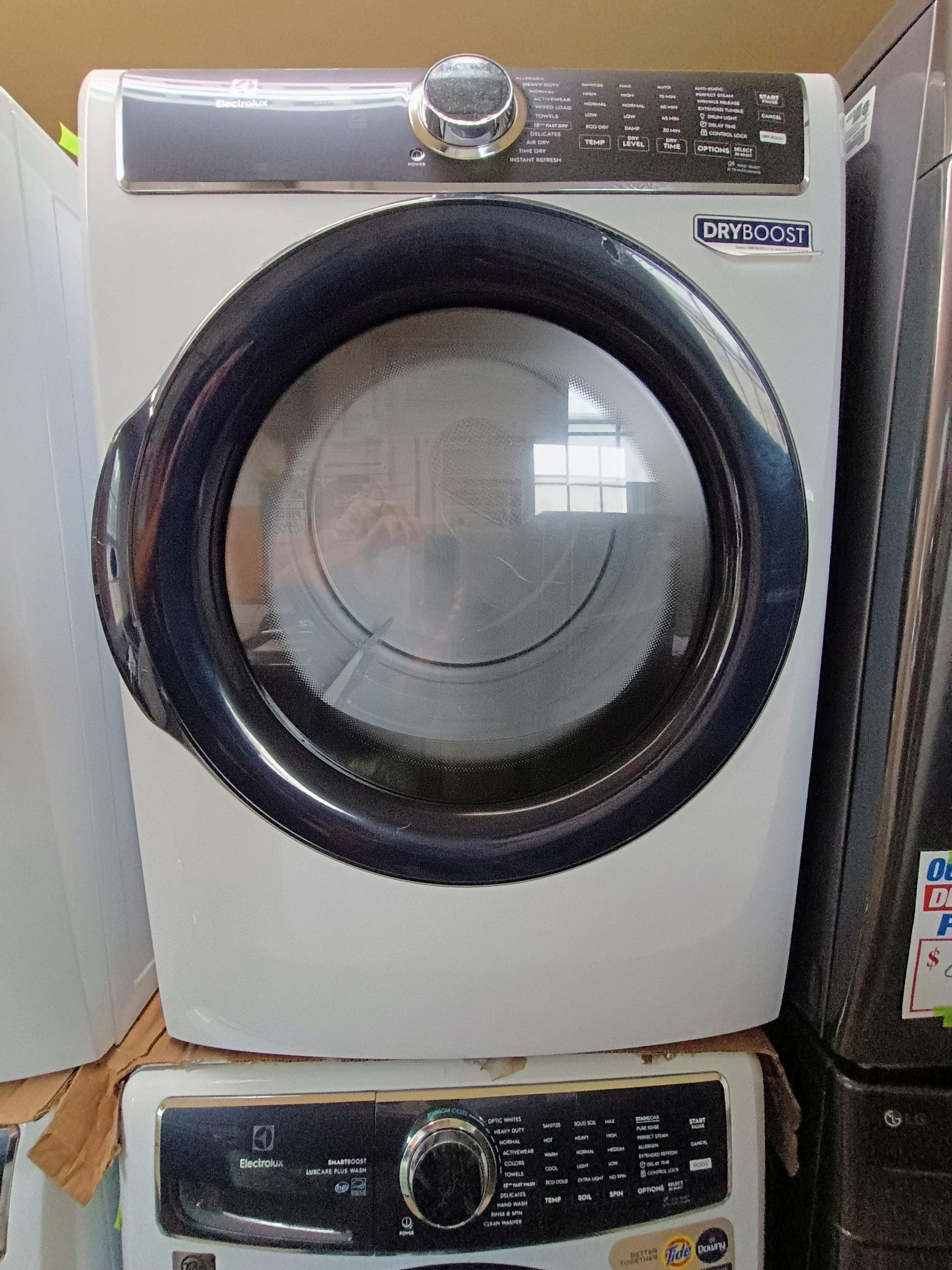 White Maytag dryer with a dark blue door ring, displayed in an appliance store.