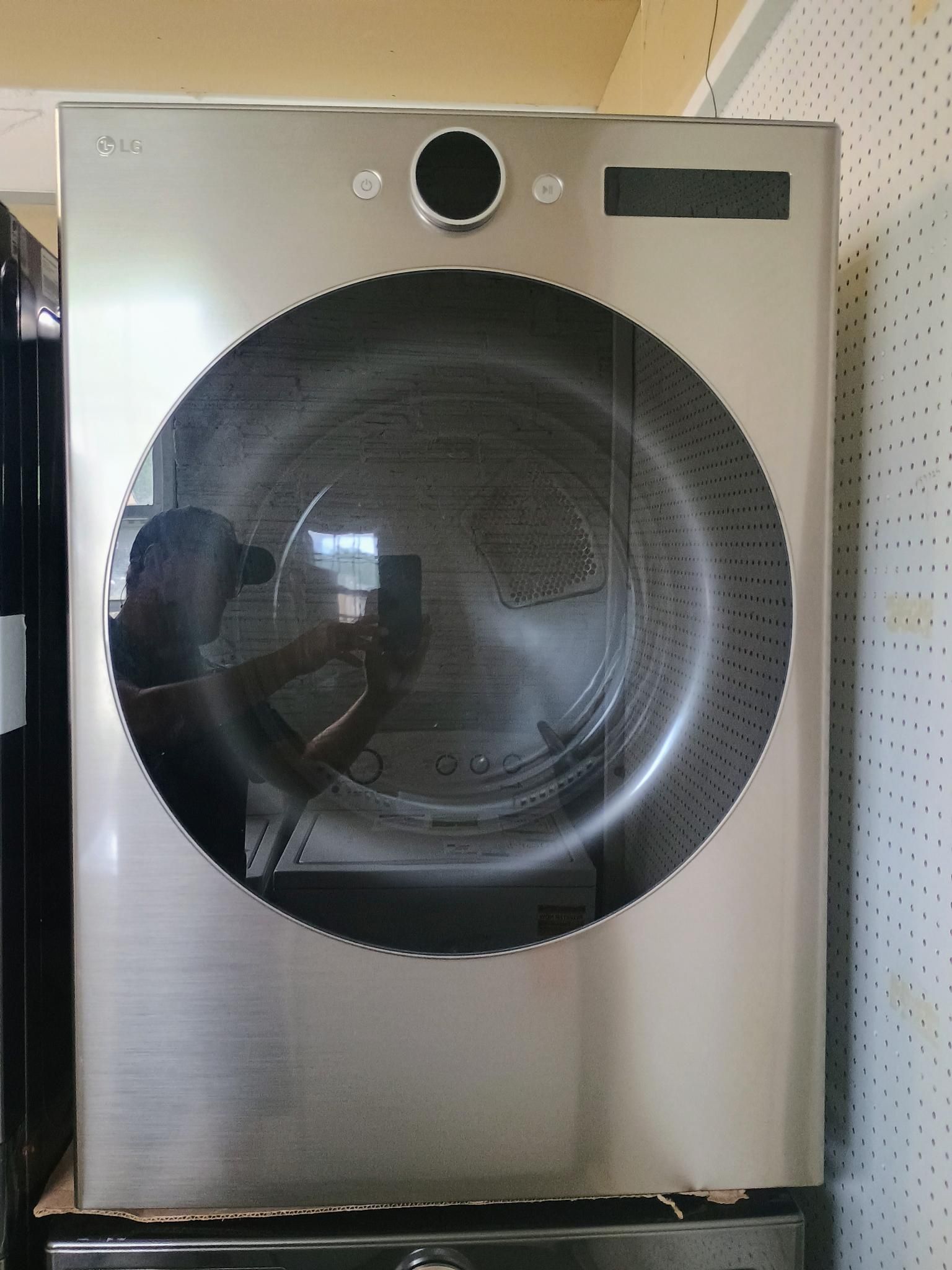 Silver LG dryer, front view, with large round door. Person visible reflected in the glass.