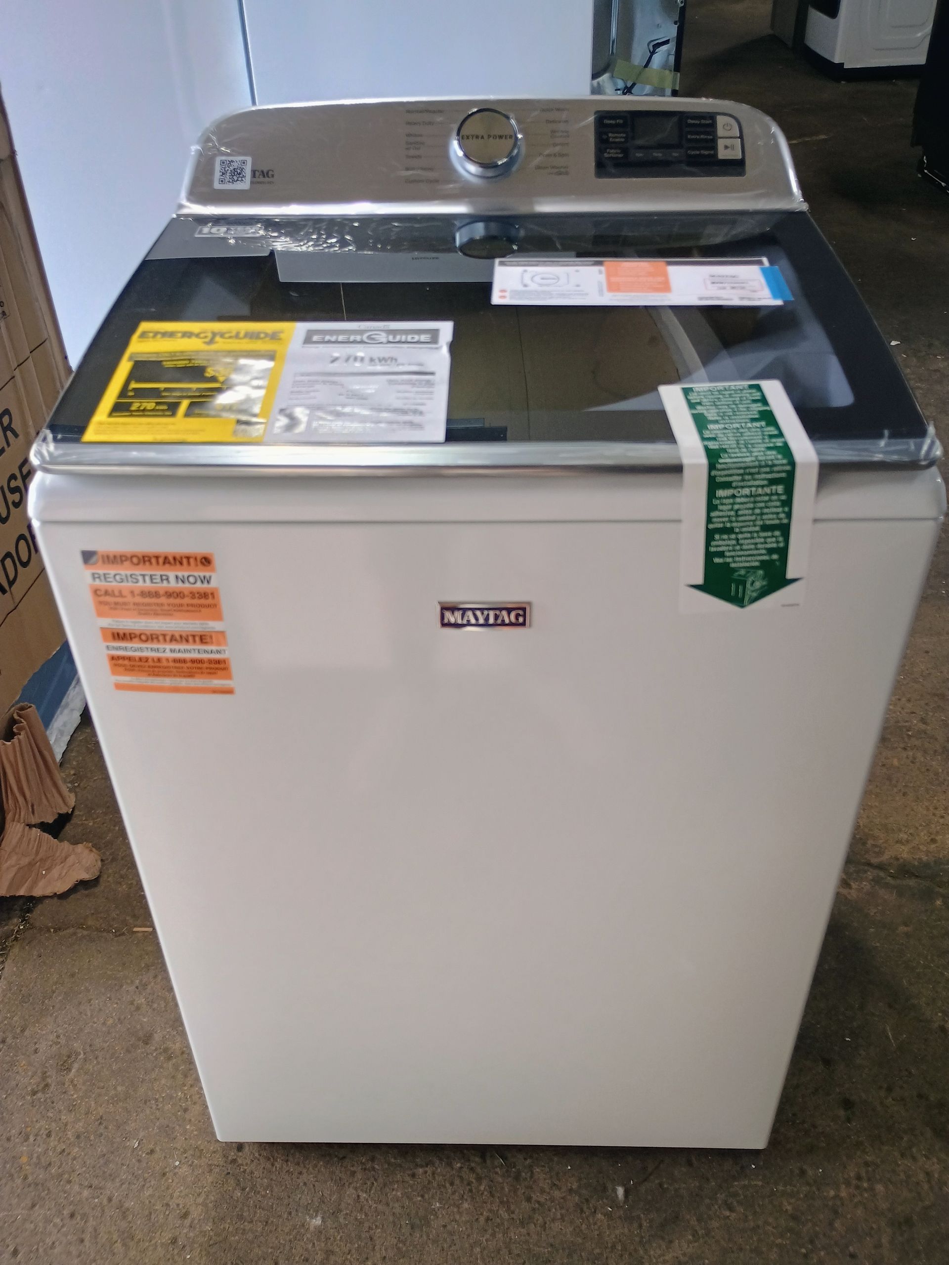 White Maytag top-load washing machine with glass lid, energy labels attached.