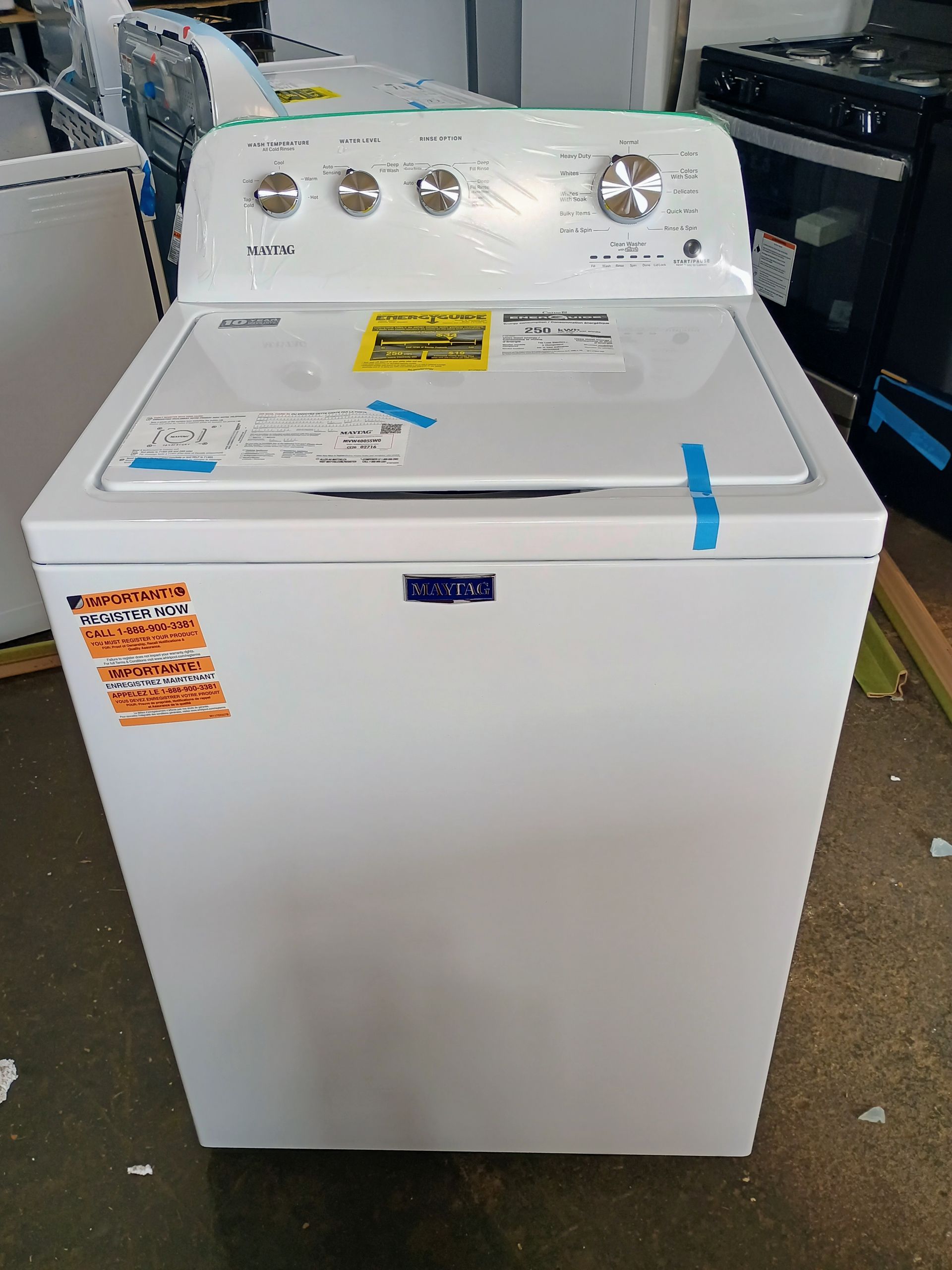 White Maytag top-load washing machine in a store, featuring control knobs and an energy guide sticker.