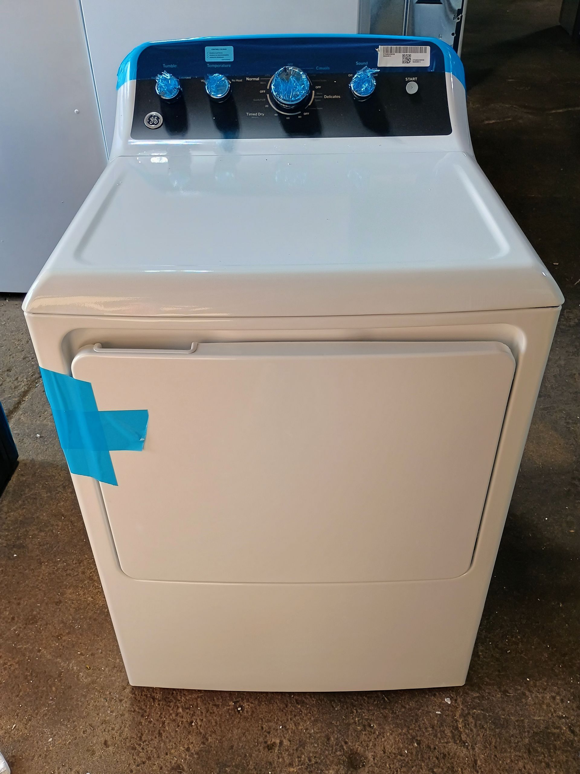 White GE electric clothes dryer with blue control panel and tape on the door.