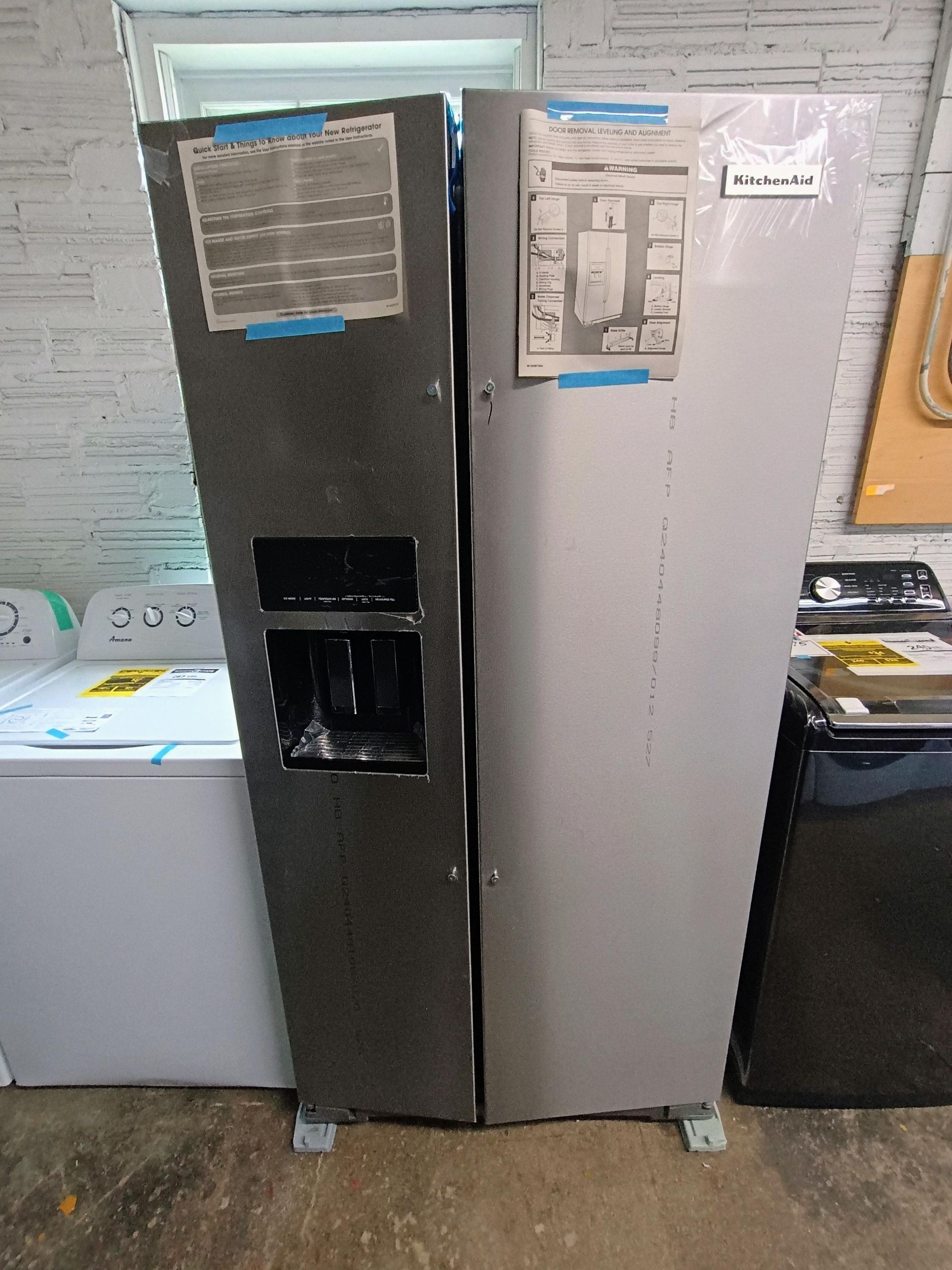 A stainless steel refrigerator is sitting in a garage next to a washer and dryer.