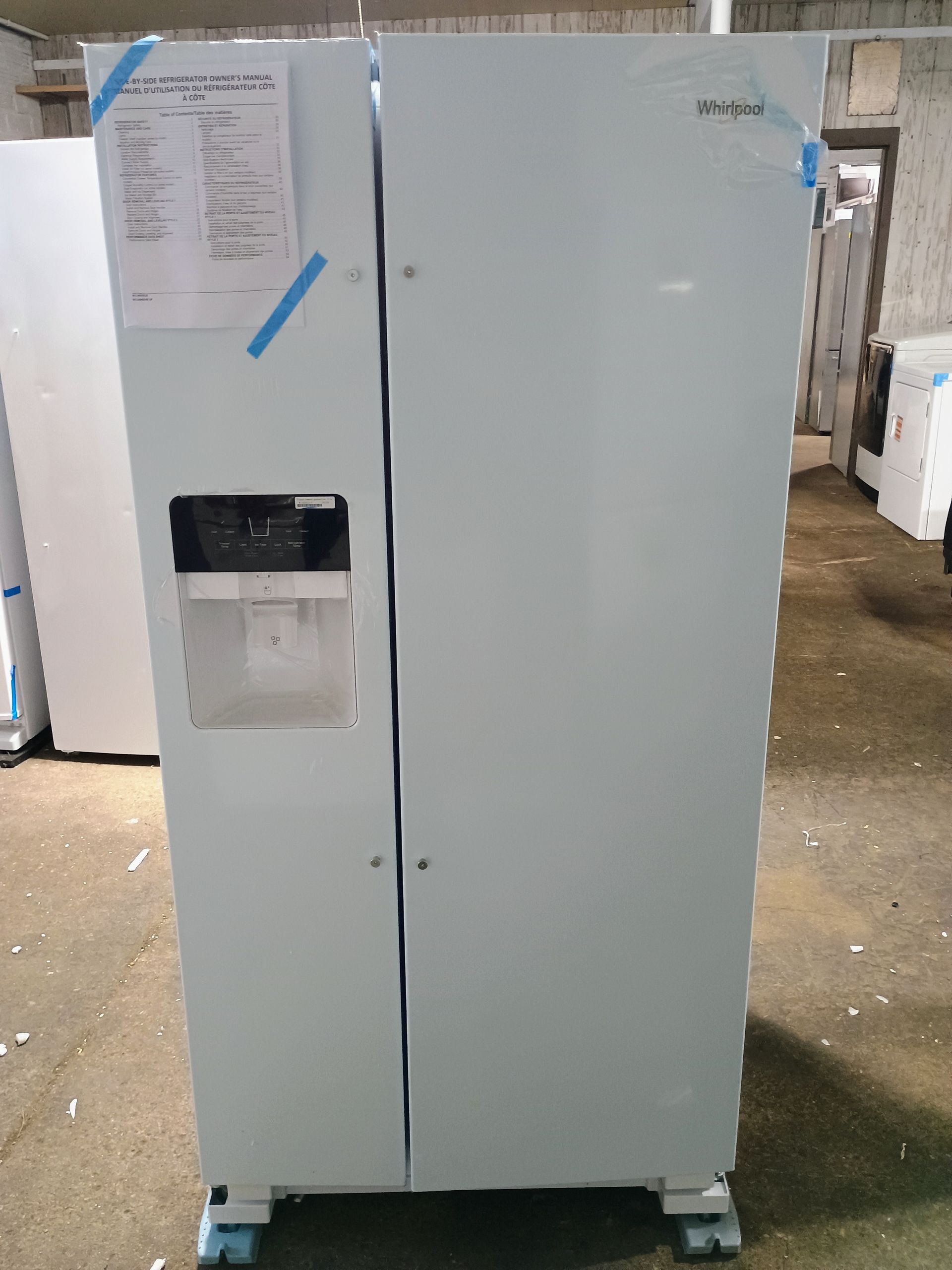 White Whirlpool side-by-side refrigerator, with ice/water dispenser. Inside a warehouse or store.
