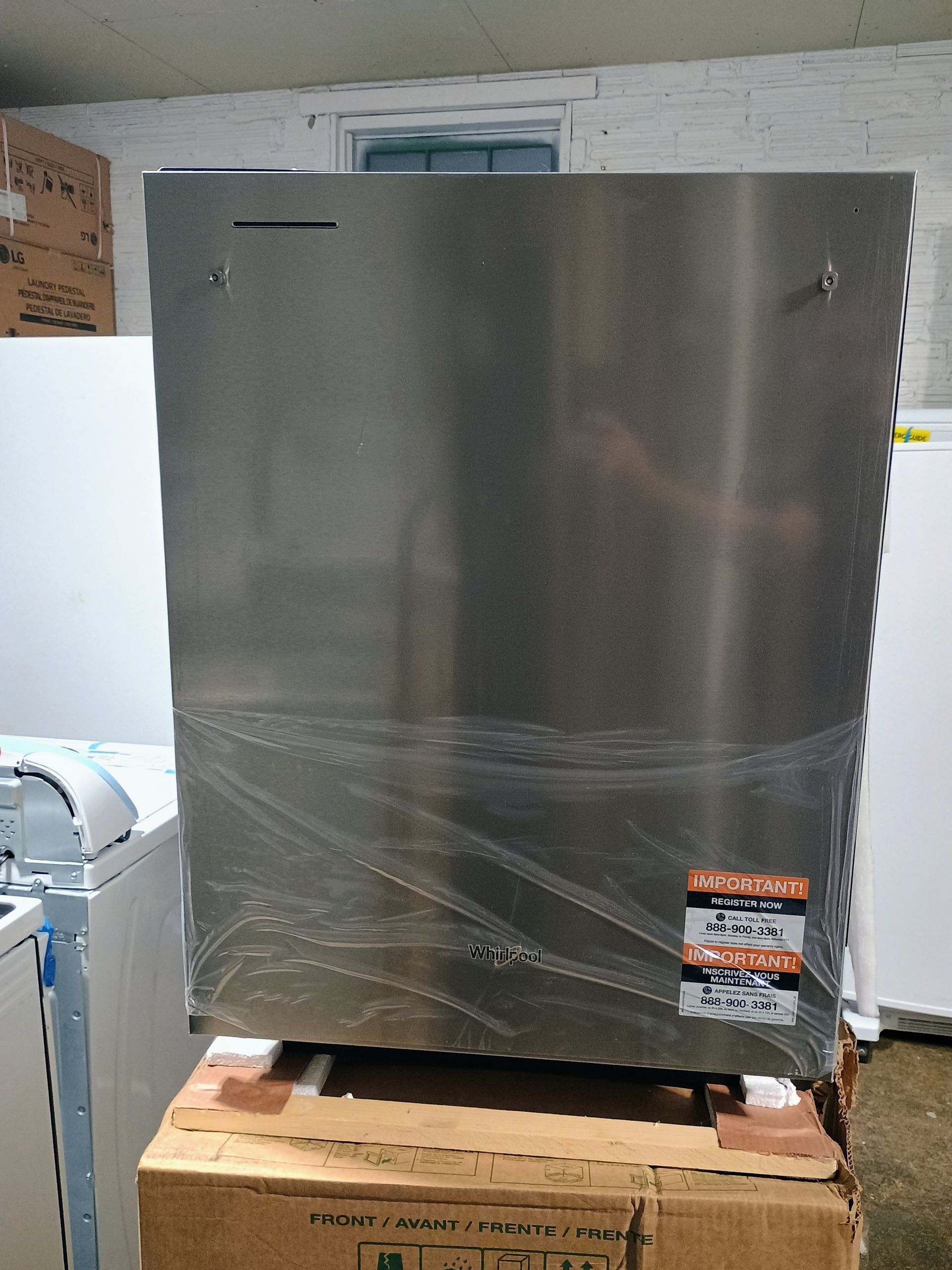 Stainless steel dishwasher on a cardboard box, wrapped in plastic.