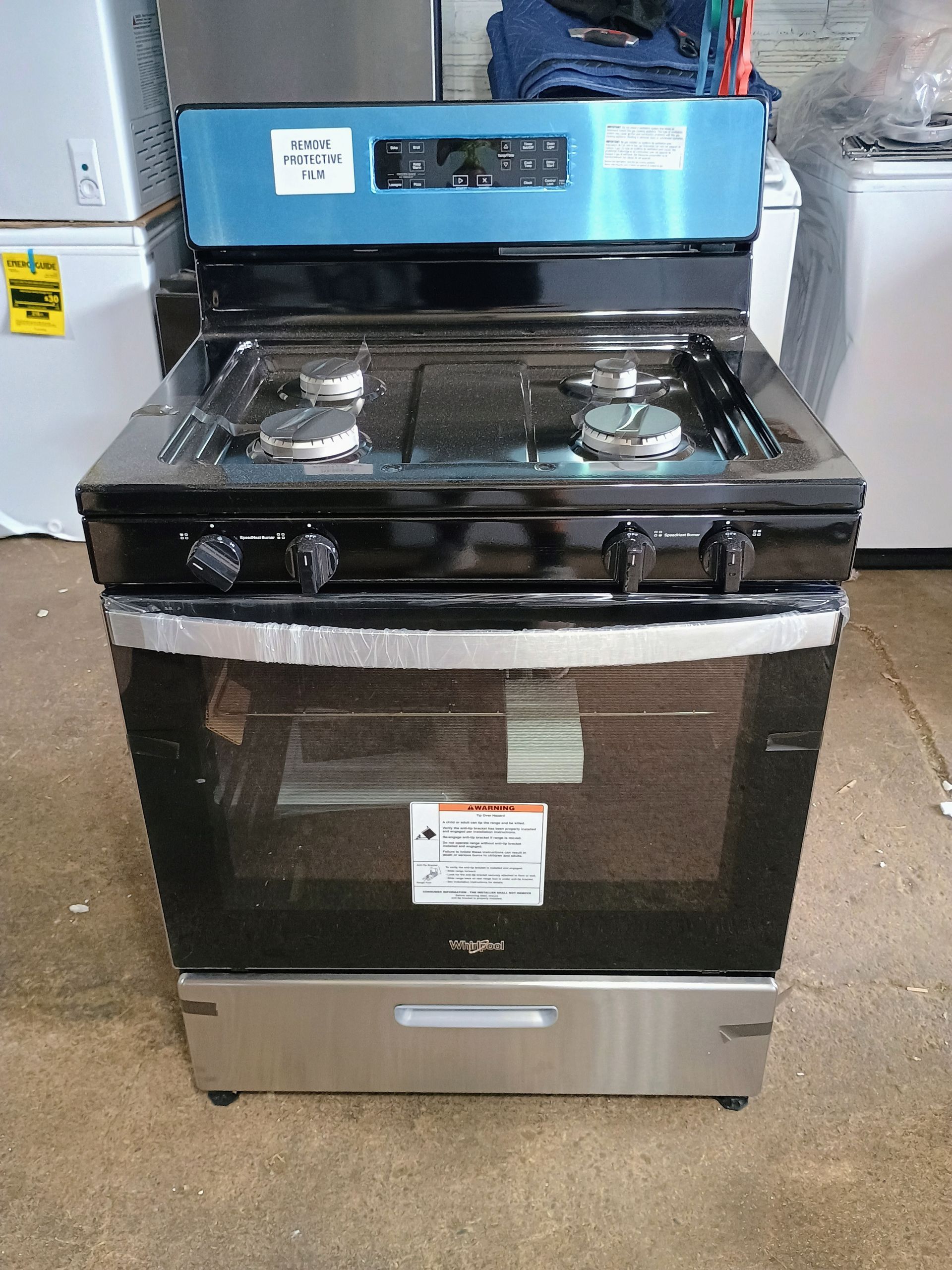 A Whirlpool gas range with a black cooktop, stainless steel base, and a blue control panel in a store.