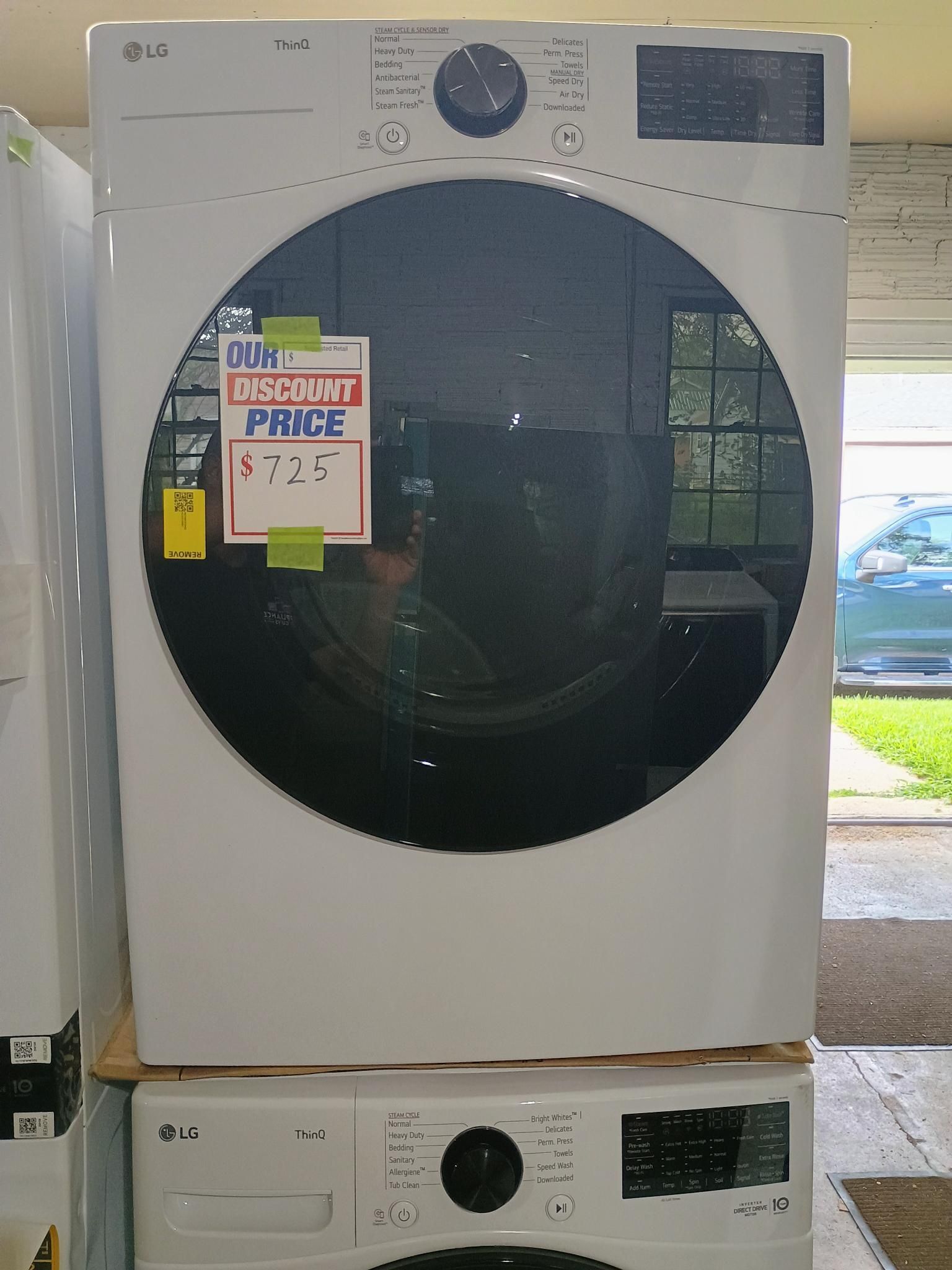 White LG dryer with large circular door, stacked on a matching washing machine. Sale sign.