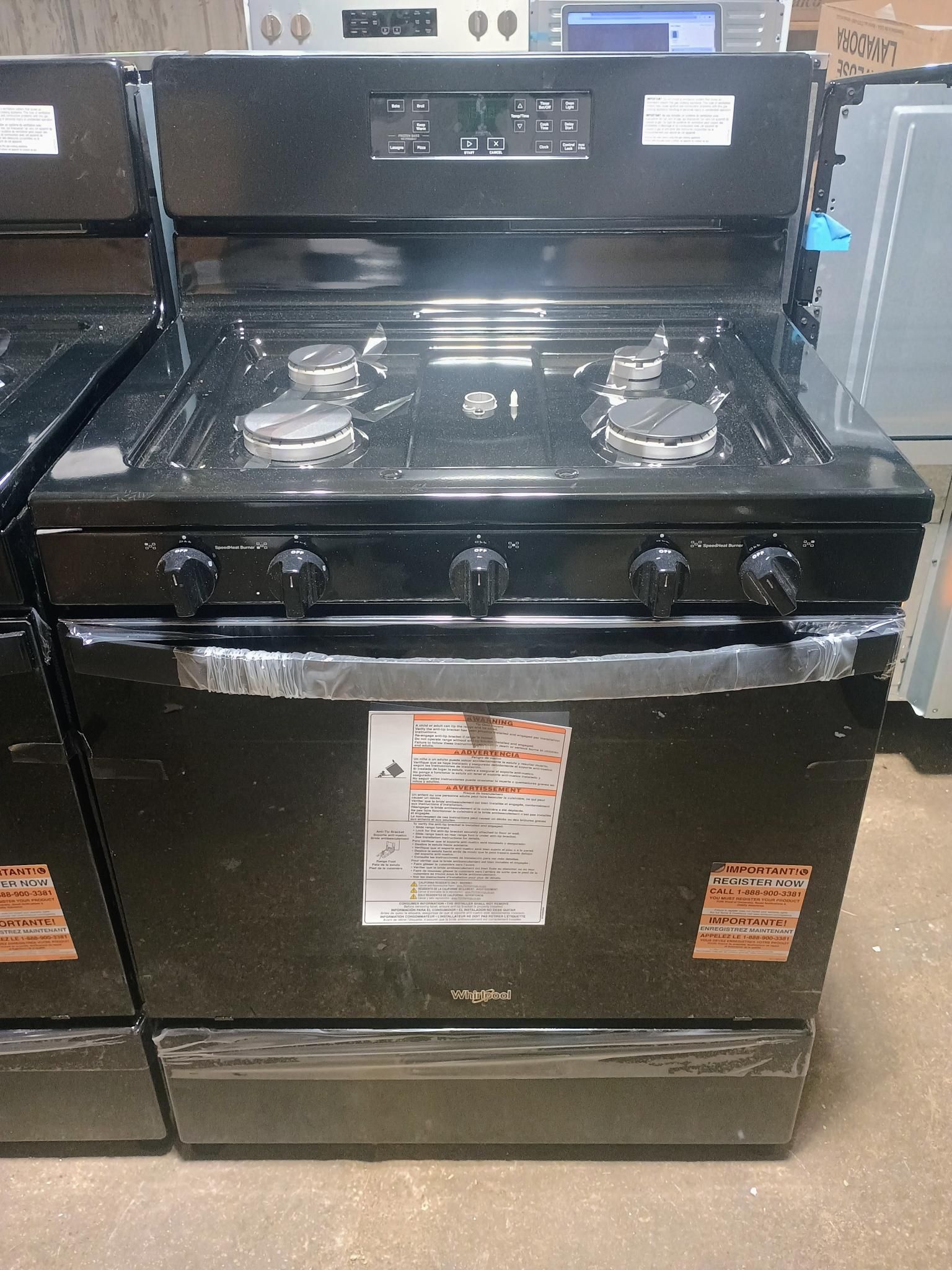 Black gas range with four burners and oven. Control panel above, storage drawer below.