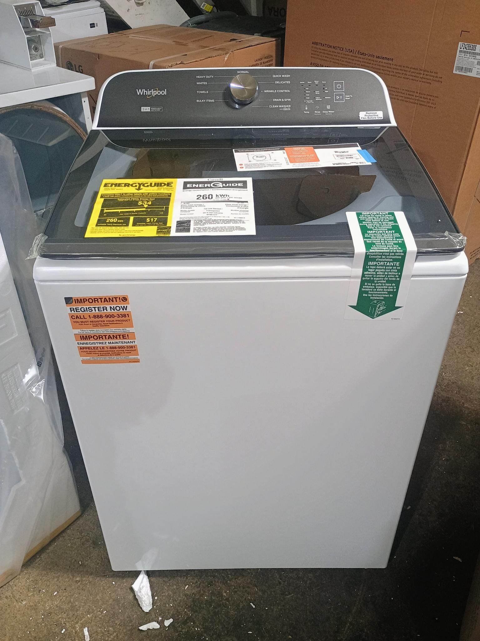 White Whirlpool top-load washing machine with a black control panel and glass lid; multiple stickers are on the appliance.