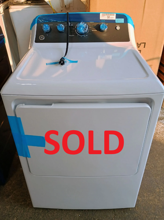 A new, white GE dryer with blue control panel tape. Front view, indoor setting.