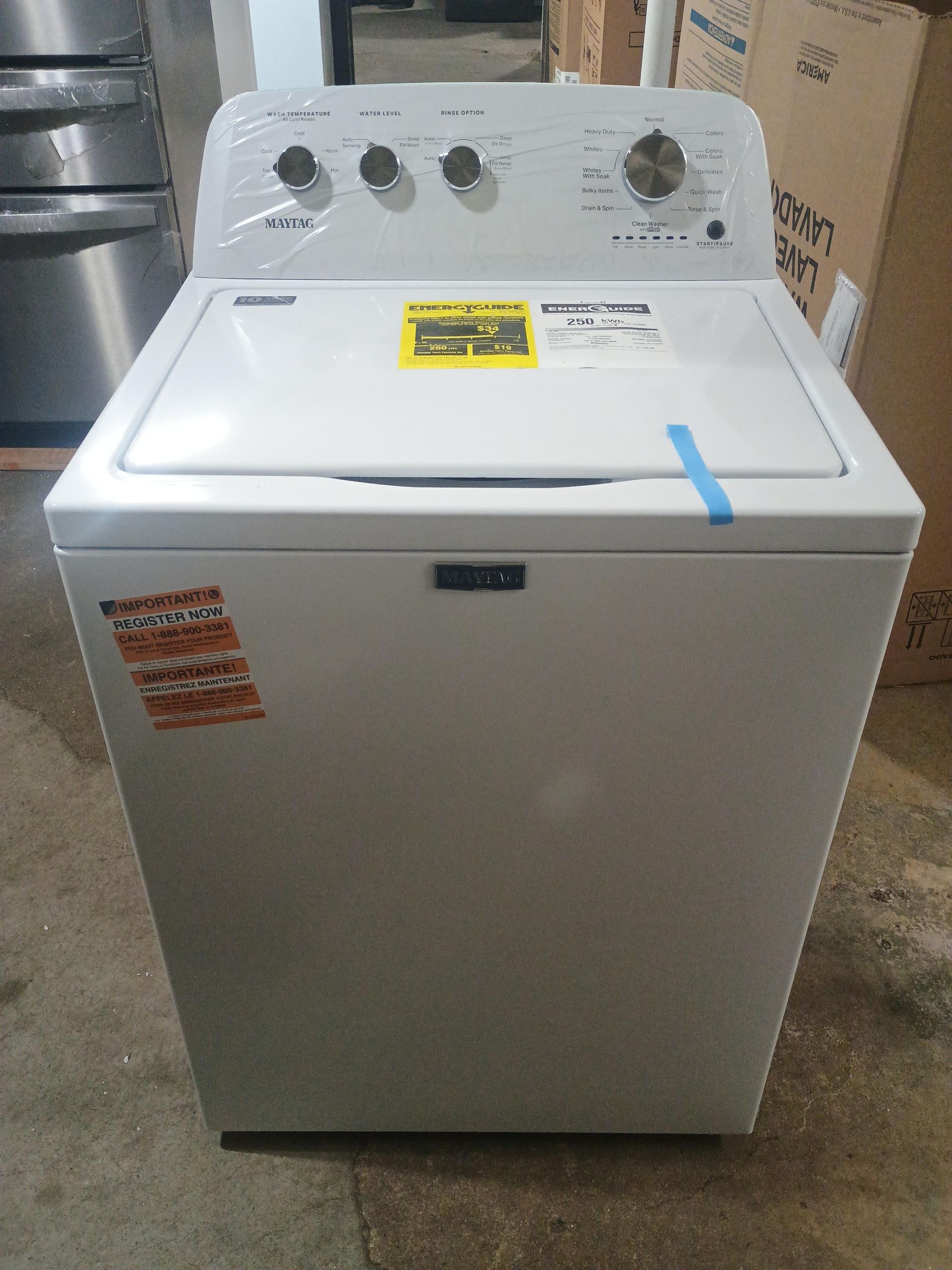White Maytag top-load washing machine with knobs on top. Black base, stickers on the front.
