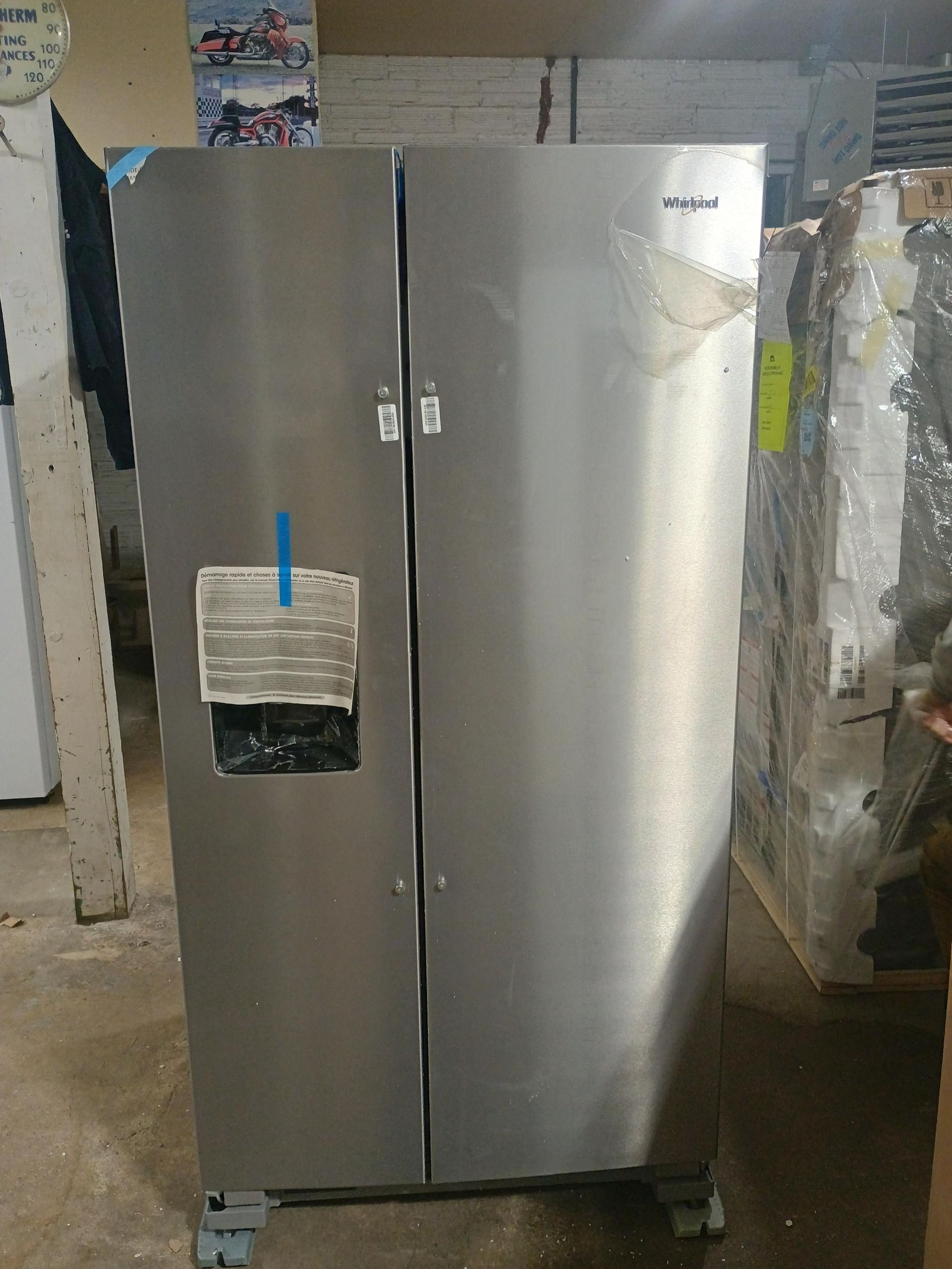 Stainless steel side-by-side refrigerator in a room. It has a water dispenser and stickers on the door.