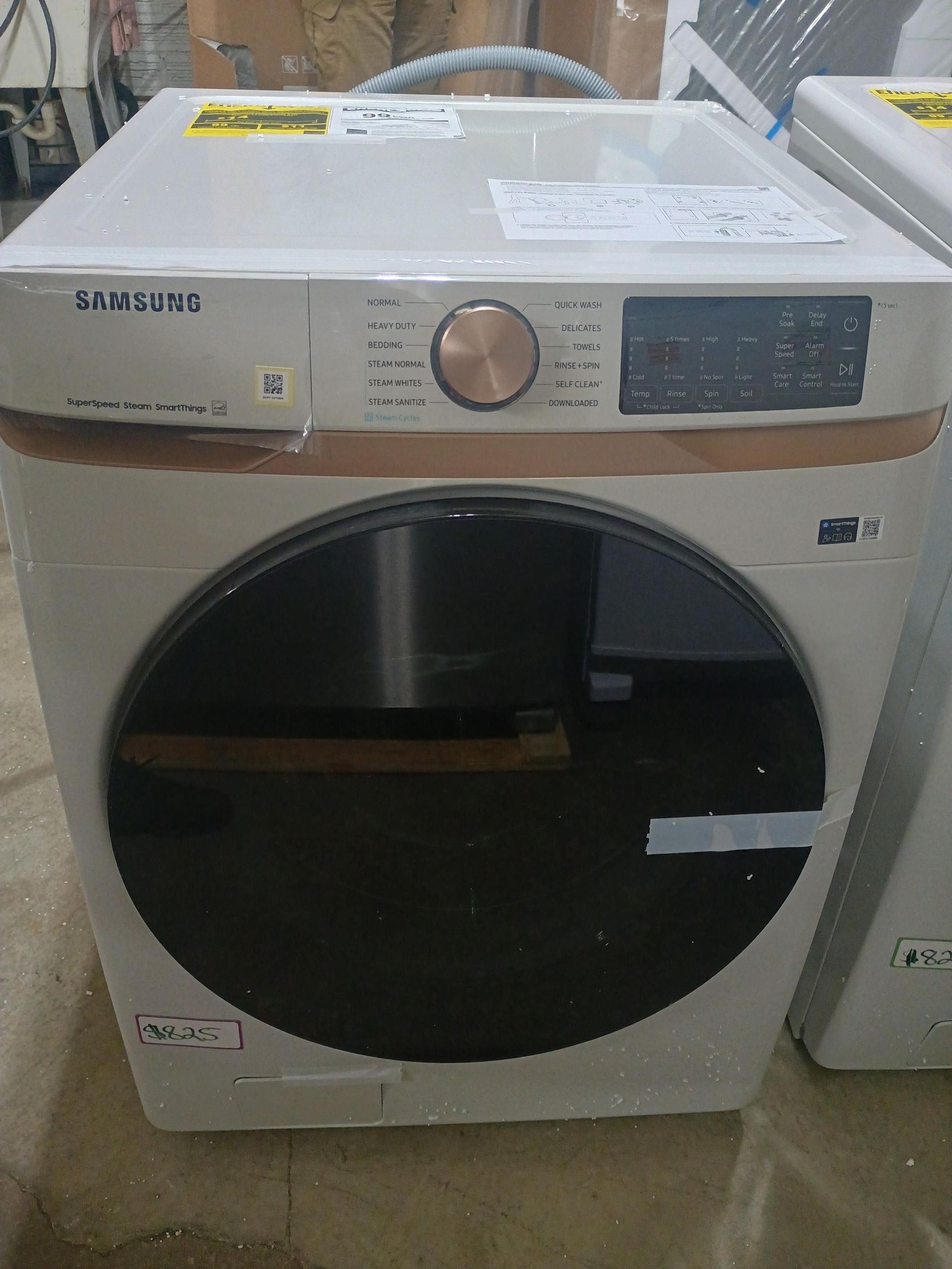 A new Samsung dryer, off-white with a dark glass door and a gold control panel.