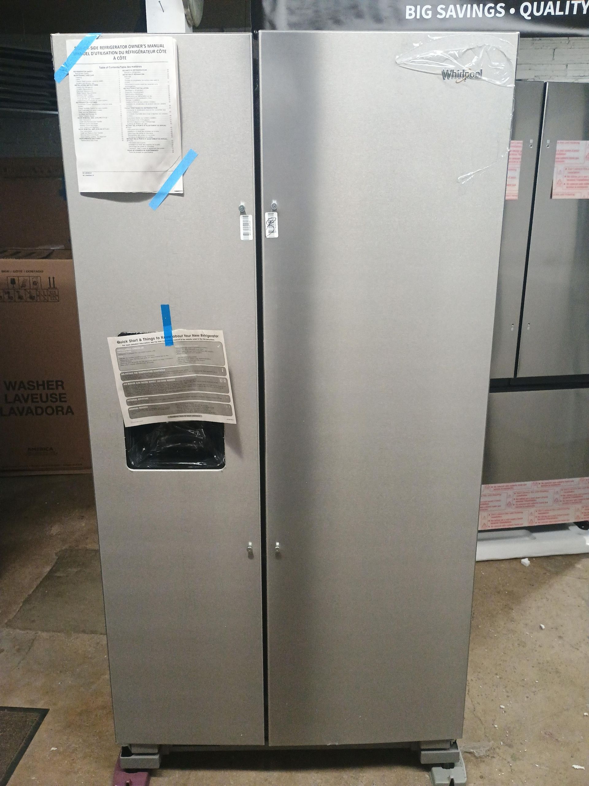 Stainless steel side-by-side refrigerator with water dispenser, sale tags attached.