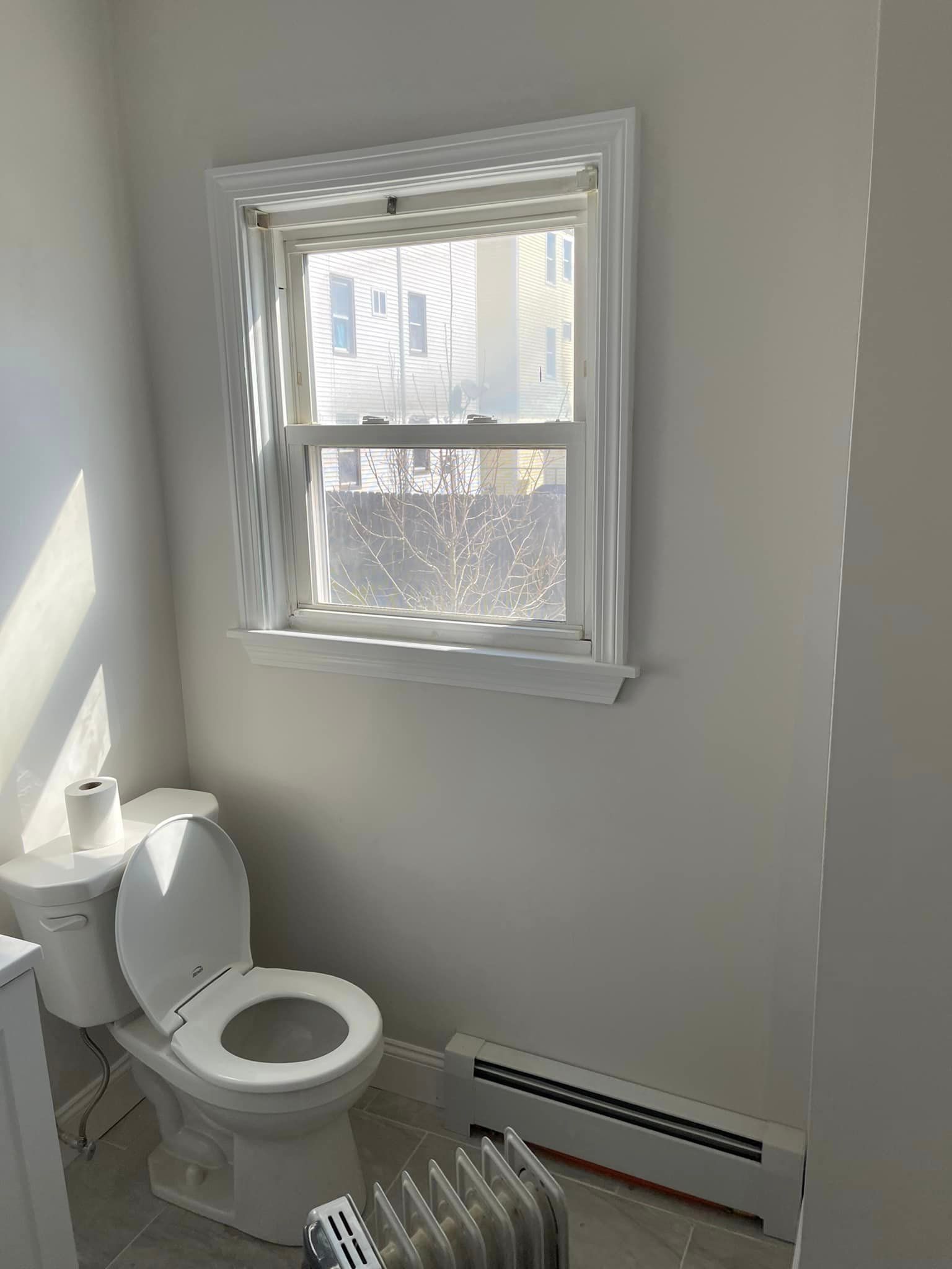 A bathroom with a toilet , radiator , and window.