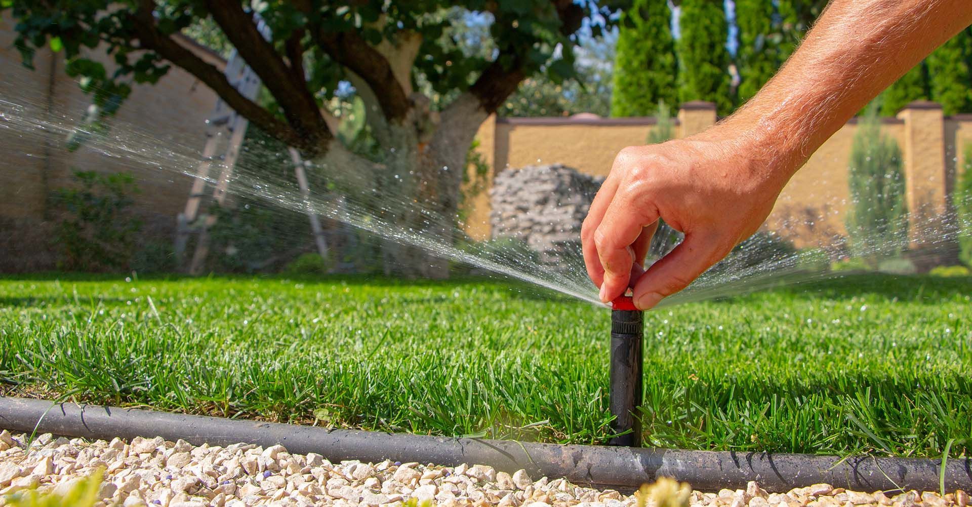 A contractor's hand manipulating an automatic sprinkler system on a background of green grass. A contractor's hand manipulating an automatic sprinkler system on a background of green grass.