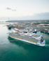 Large white cruise ship docked in a turquoise harbor beside a coastal city at sunrise.