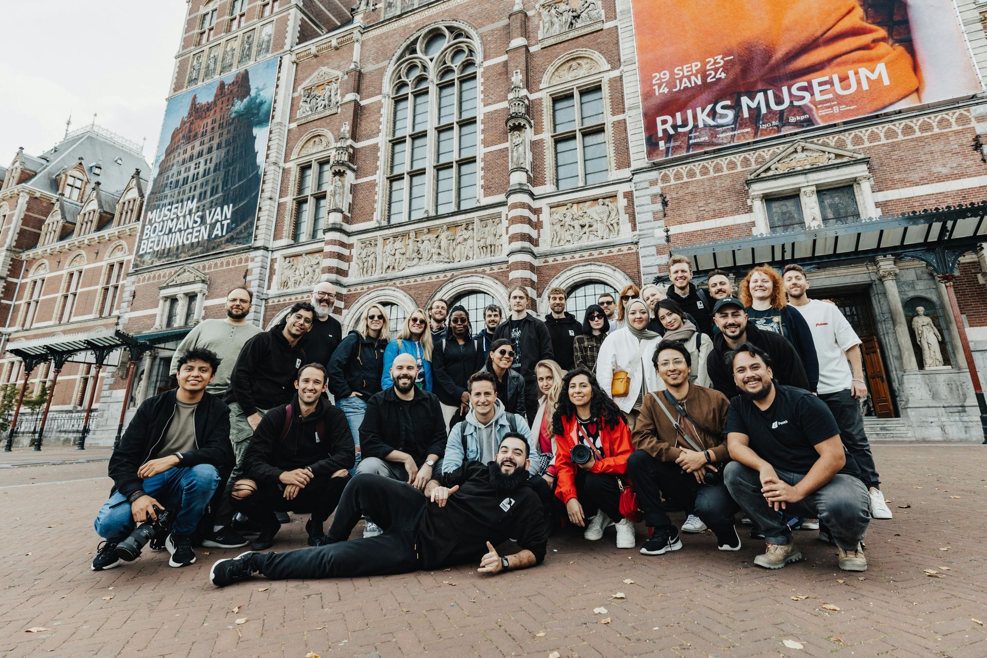 Large group posing outside the Rijksmuseum in front of brick Gothic architecture and museum signage