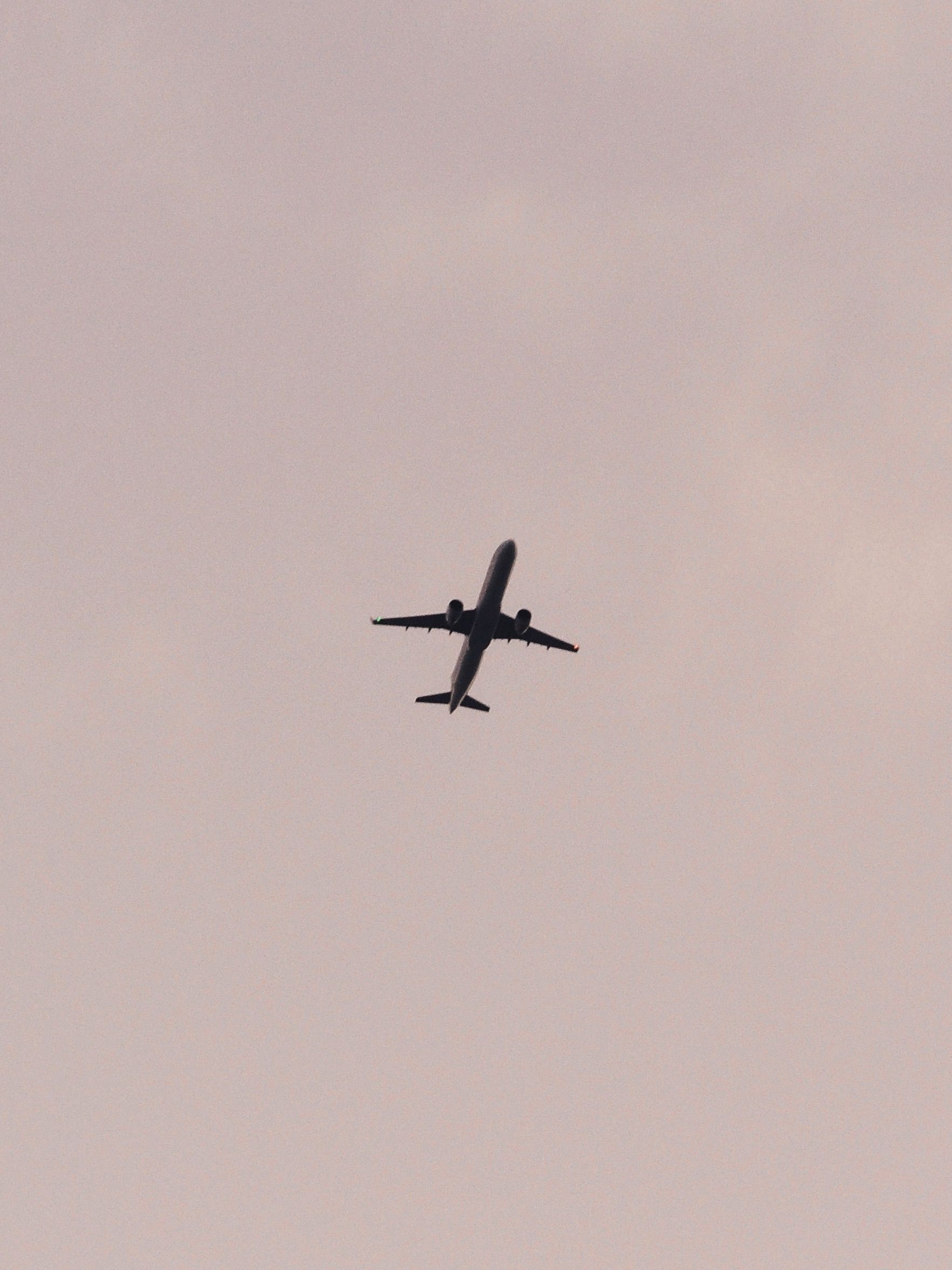 Silhouette of an airplane flying against a pale pink sky