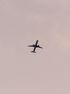 Silhouette of an airplane flying against a pale pink sky