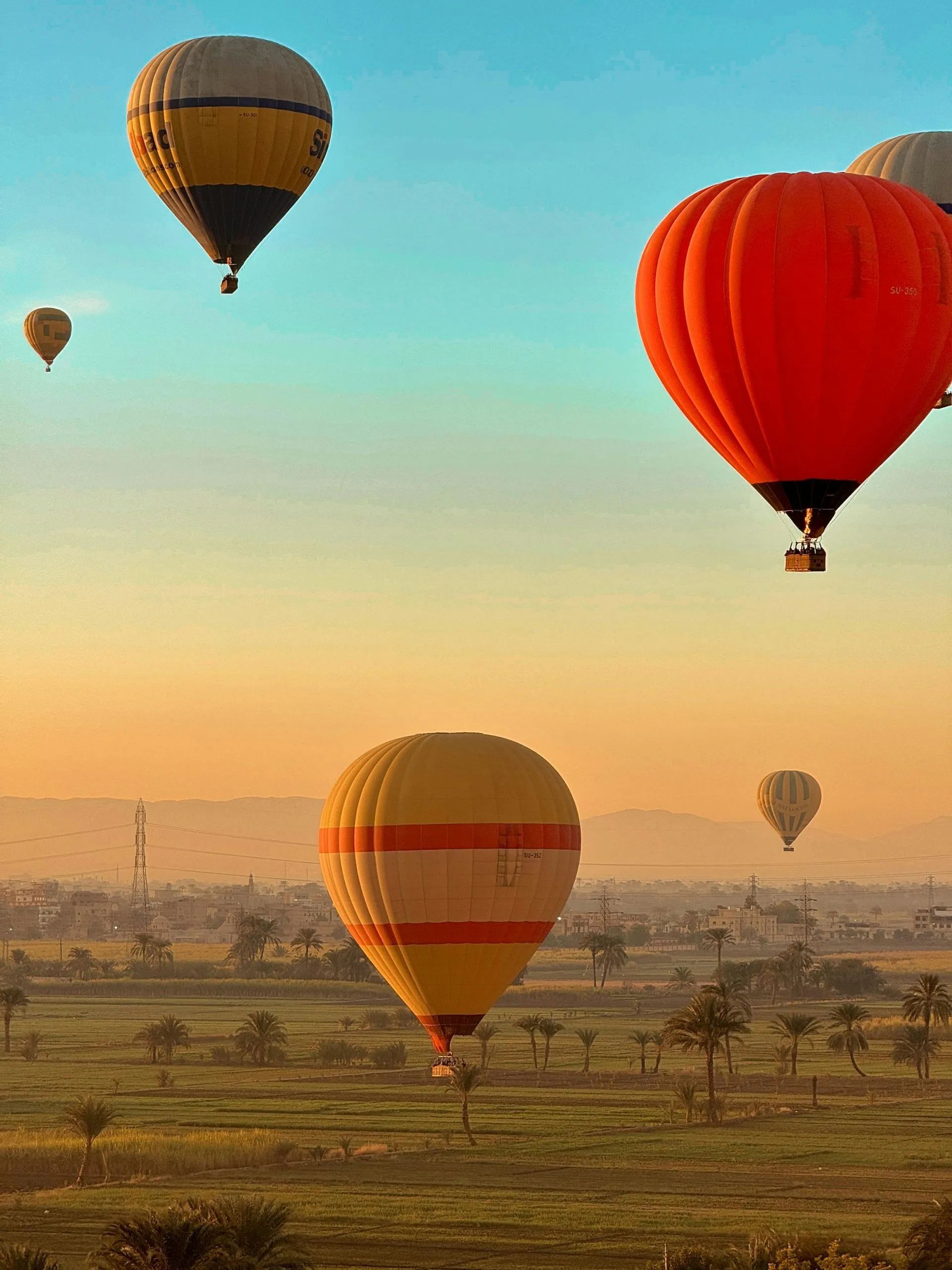 Hot air balloons float over a sunrise landscape, including a large red balloon and a striped orange balloon.