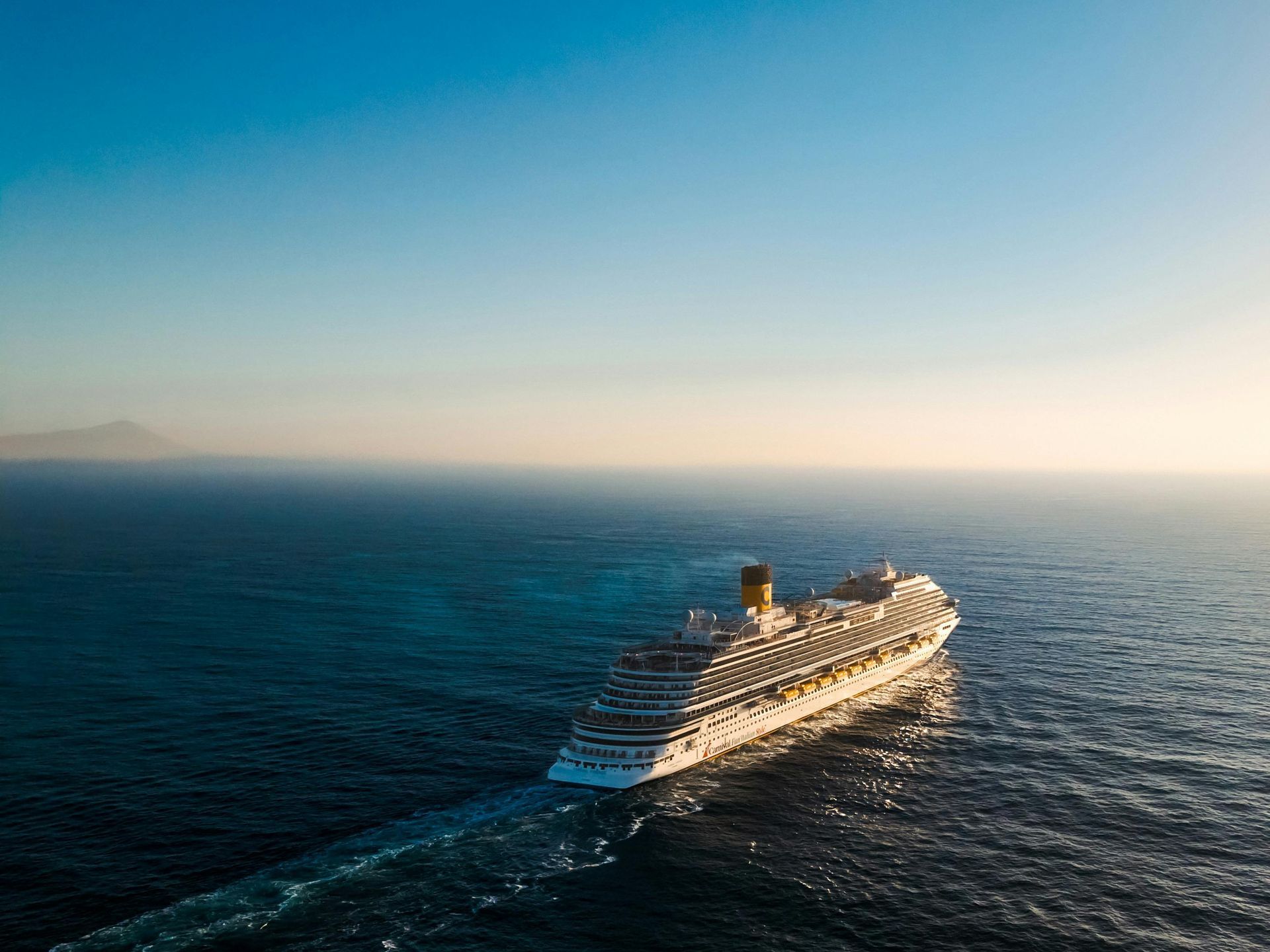 Cruise ship sailing on a calm blue ocean at sunset with a hazy coastline in the distance