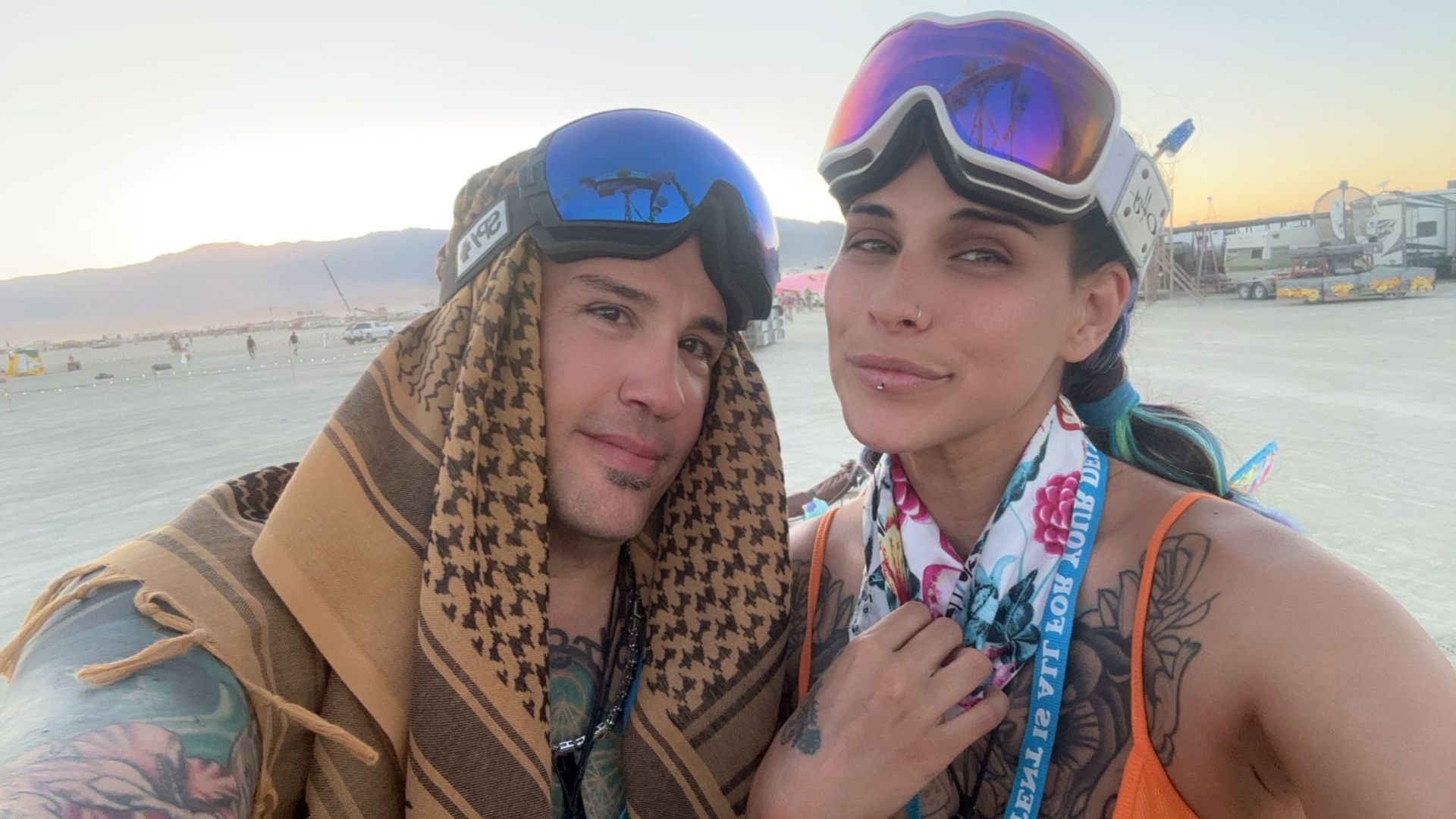 Two people wearing goggles, scarves, and desert attire posing outdoors.