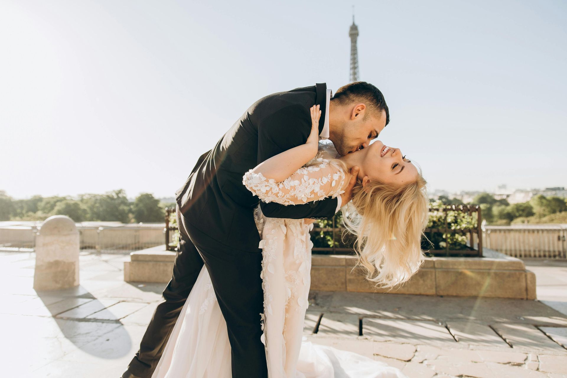 Groom dips bride, kissing her neck, with Eiffel Tower in background.