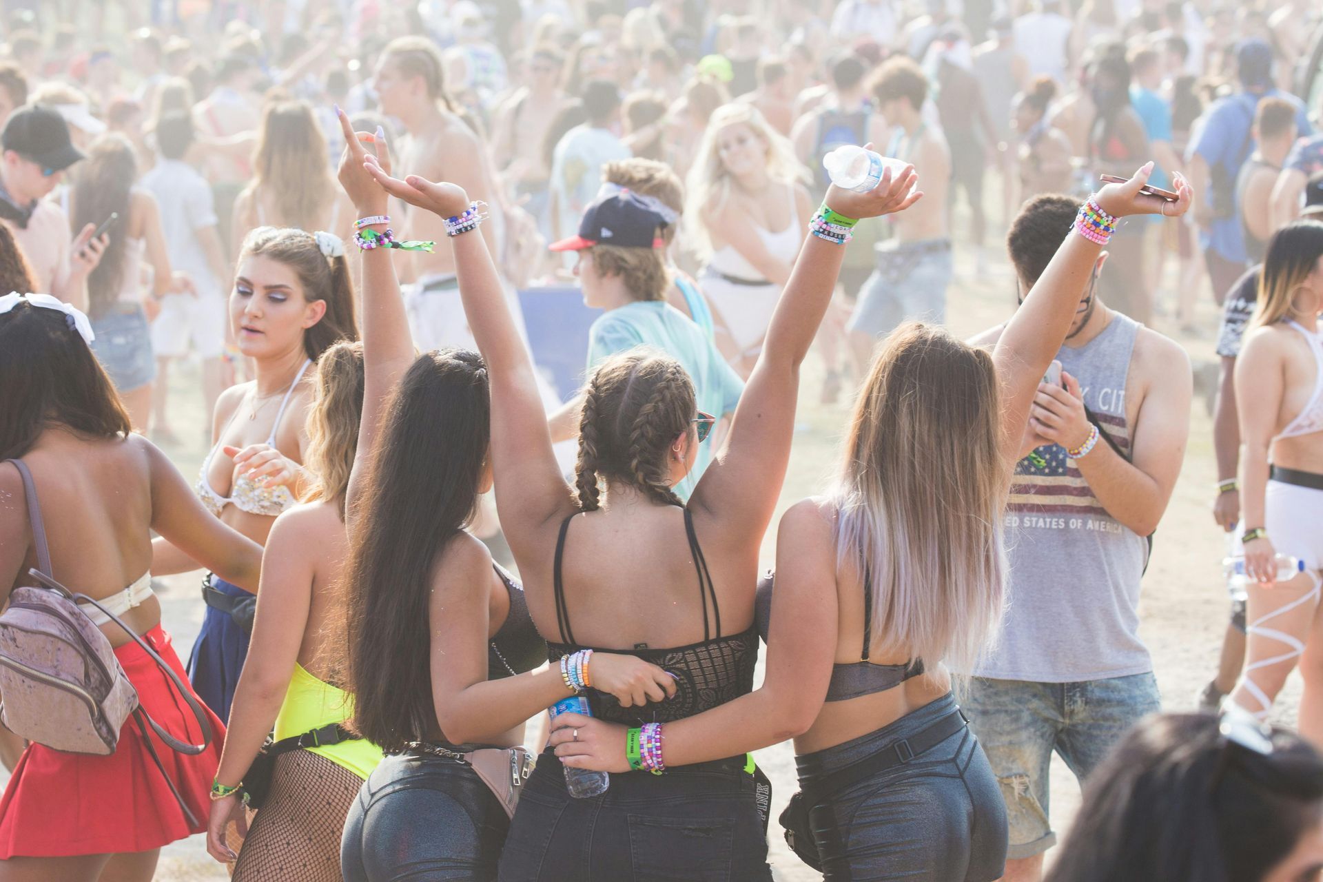 People at a music festival, arms raised, embracing. Sunny day, crowd of people.