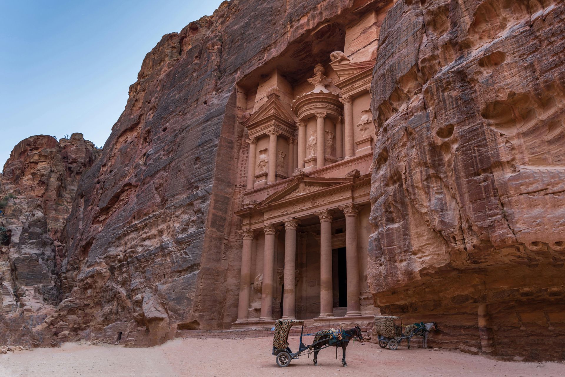 Petra's Treasury facade carved into sandstone cliffs; horse-drawn cart in front.