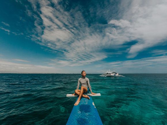 Woman sitting on a boat looking at the ocean, with blue water and cloudy sky.