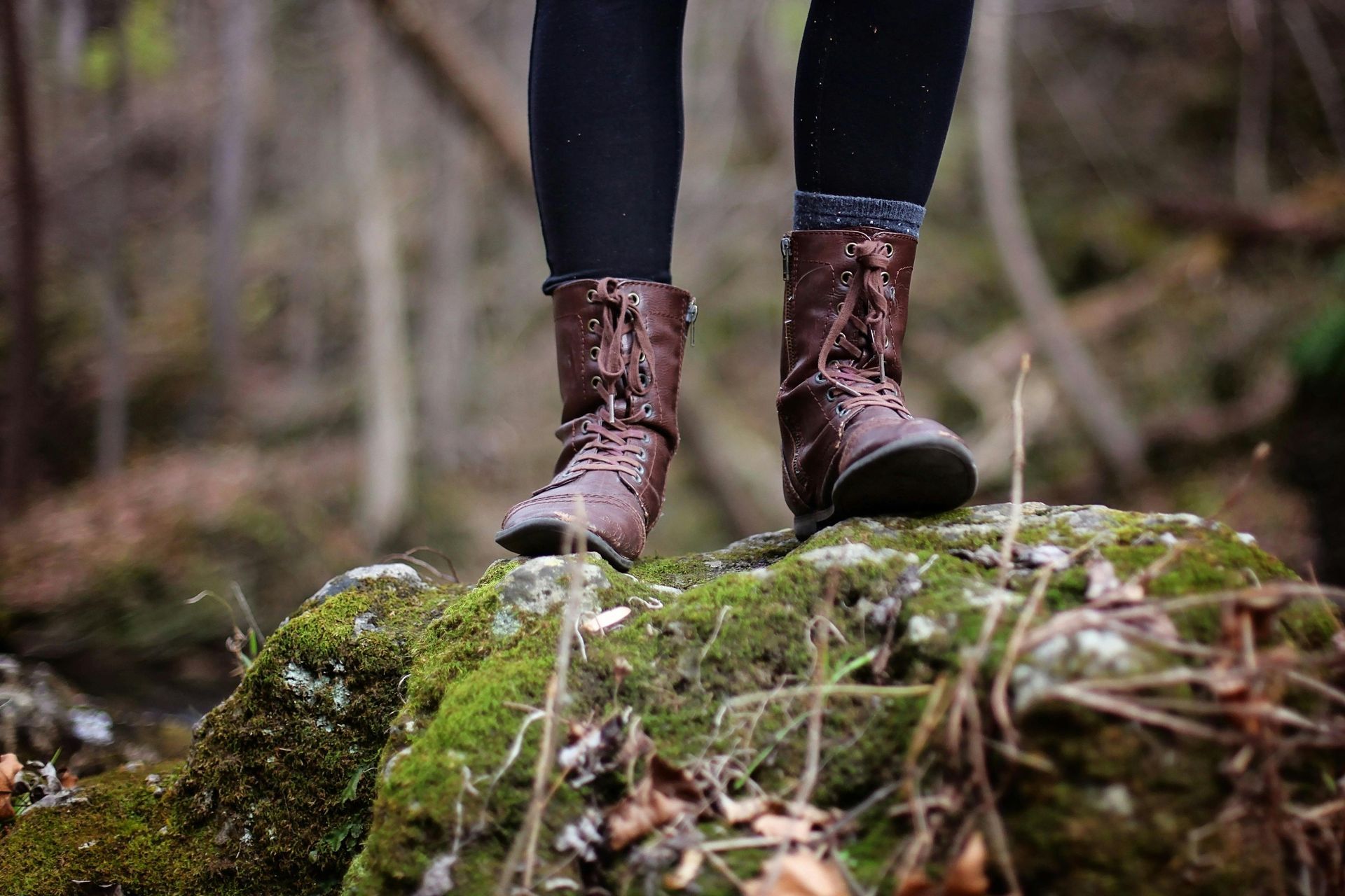 Person wearing brown boots stands on a mossy rock in a forest.