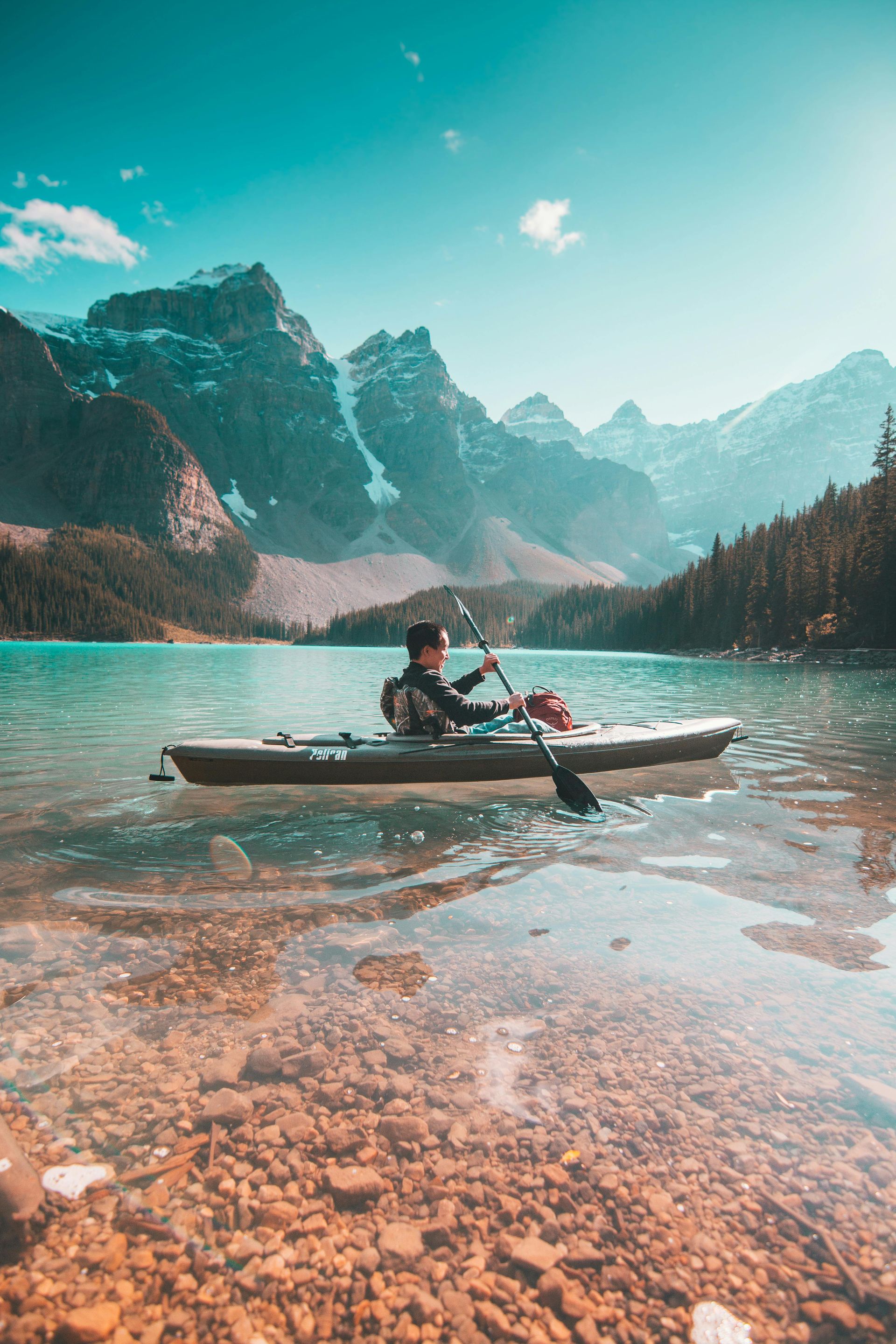 Person kayaking on turquoise lake with mountains in background.