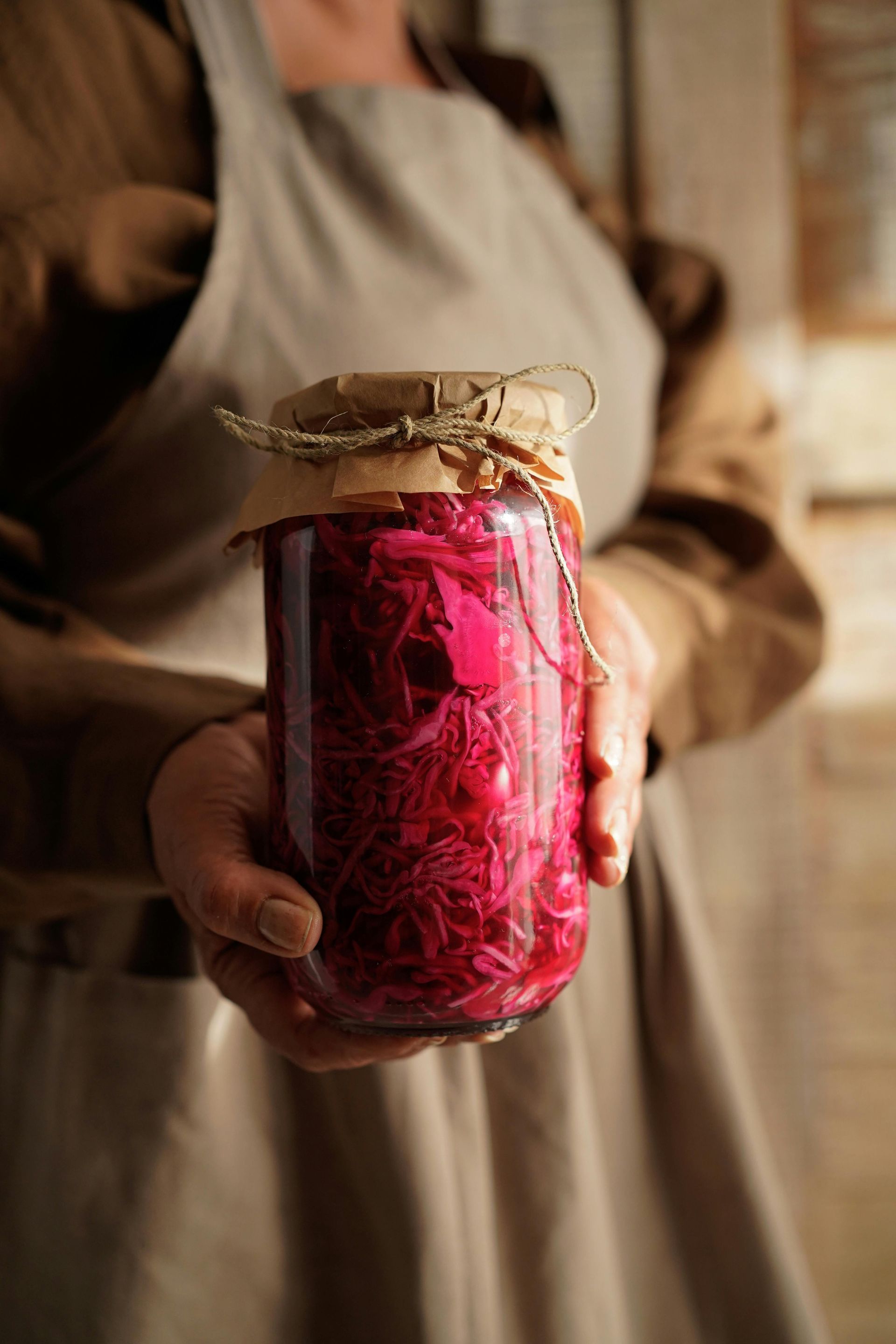 Person holding a jar of pickled red cabbage, sealed with a brown lid and twine.
