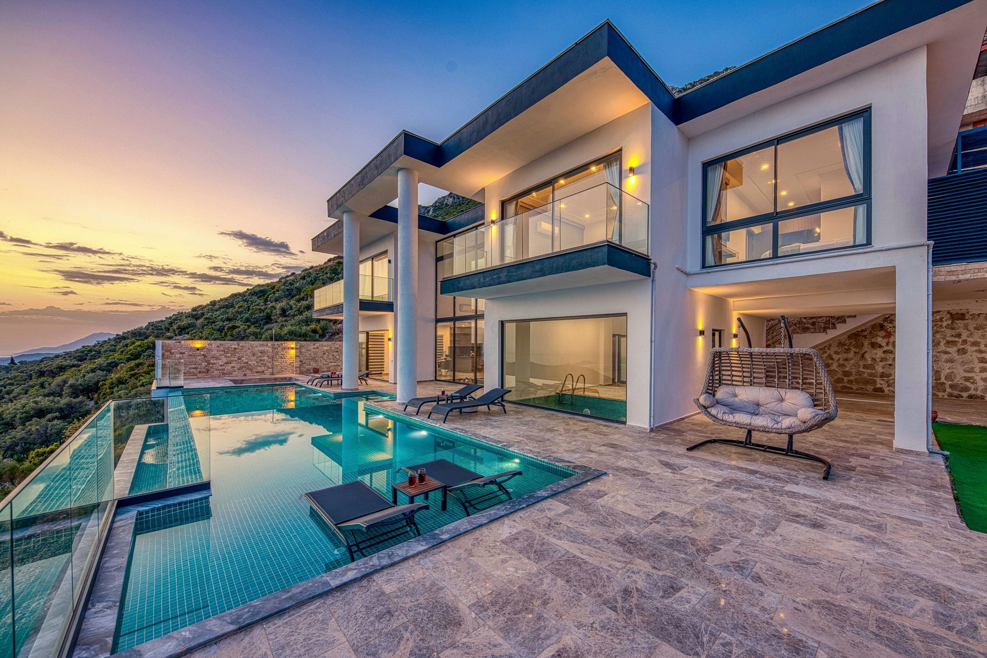 Modern villa with infinity pool overlooking the ocean at sunset.