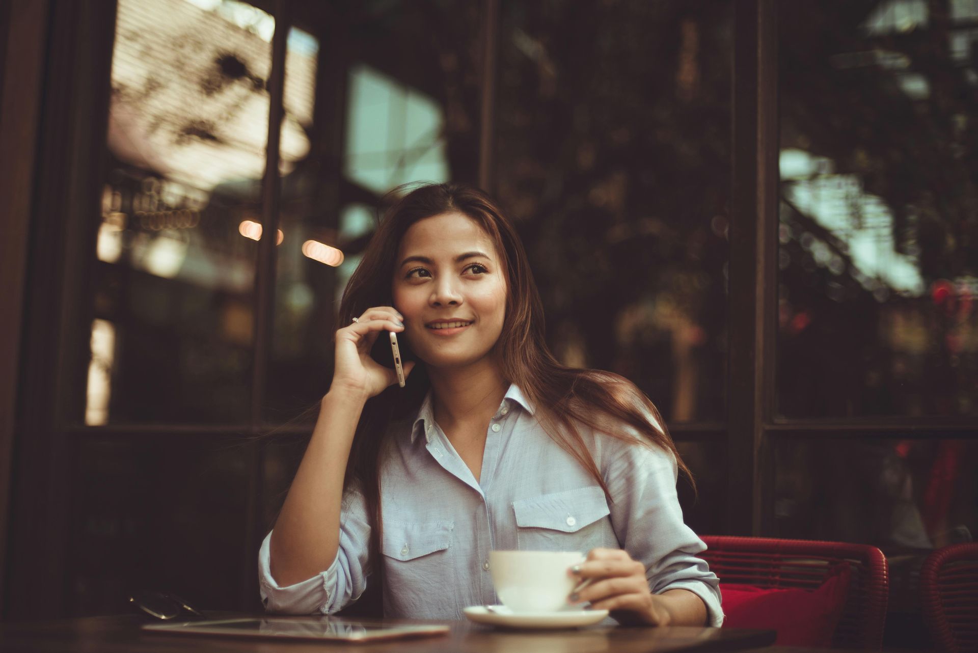 Woman in a cafe talking on the phone, holding a coffee cup, looking out the window.