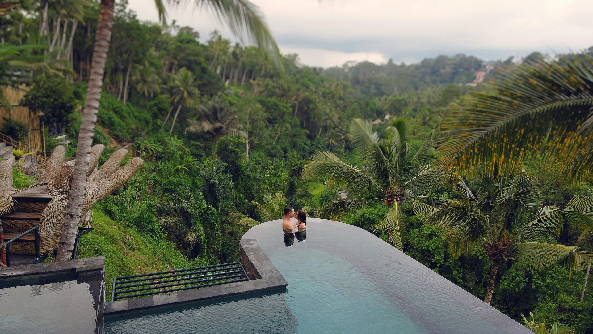 Couple standing at the edge of an infinity pool overlooking lush green tropical landscape.