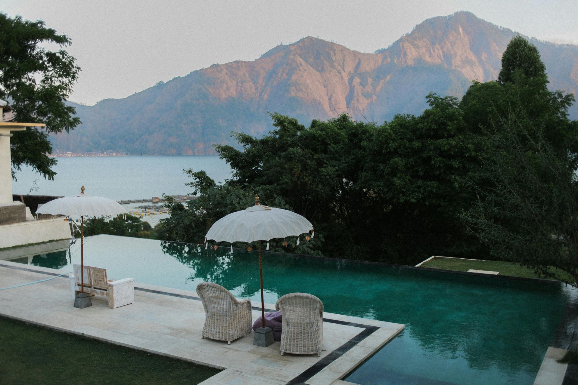 Infinity pool overlooking lake and mountains, with parasols and lounge chairs on the side.