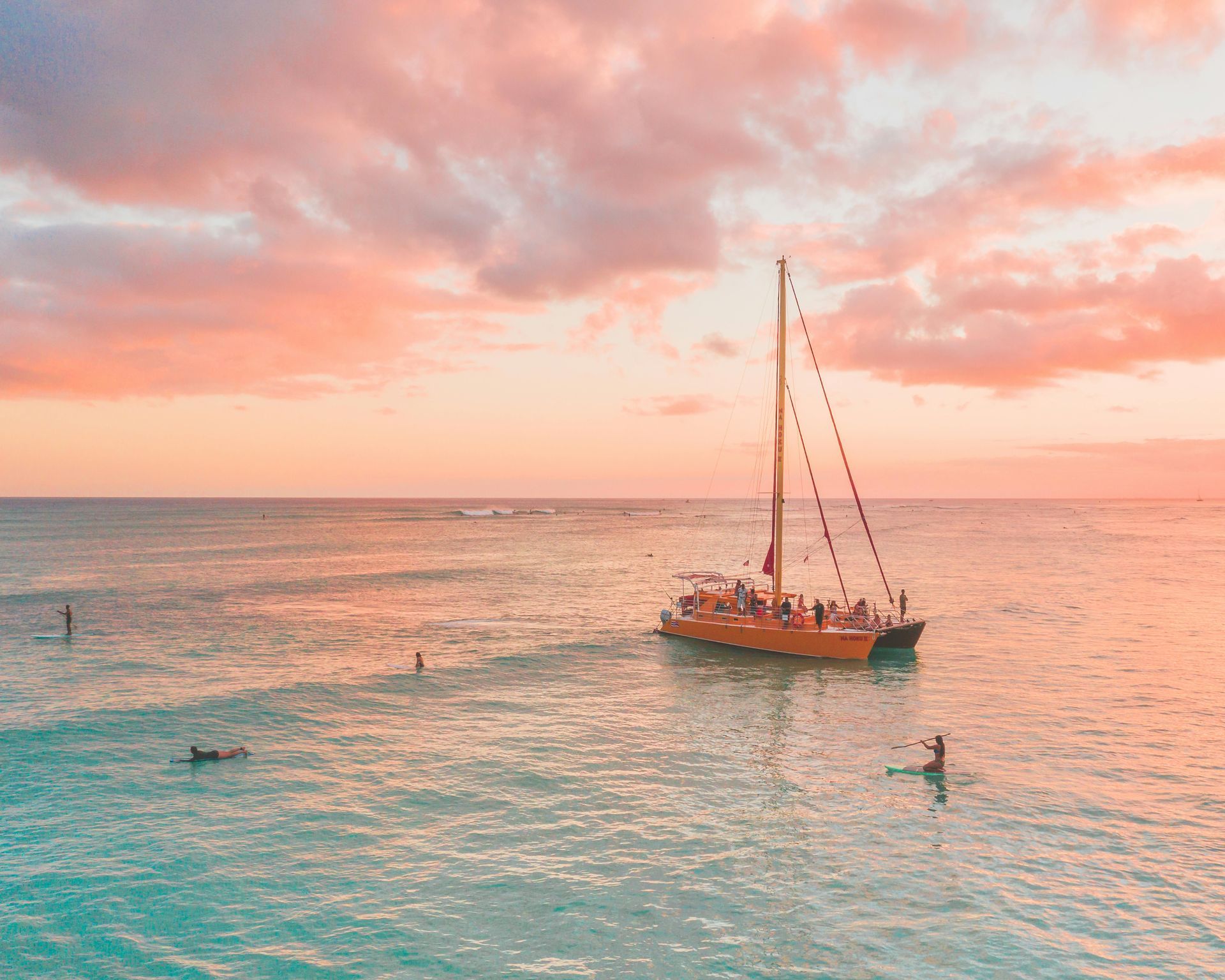 Sunset over ocean with orange sailboat and people.