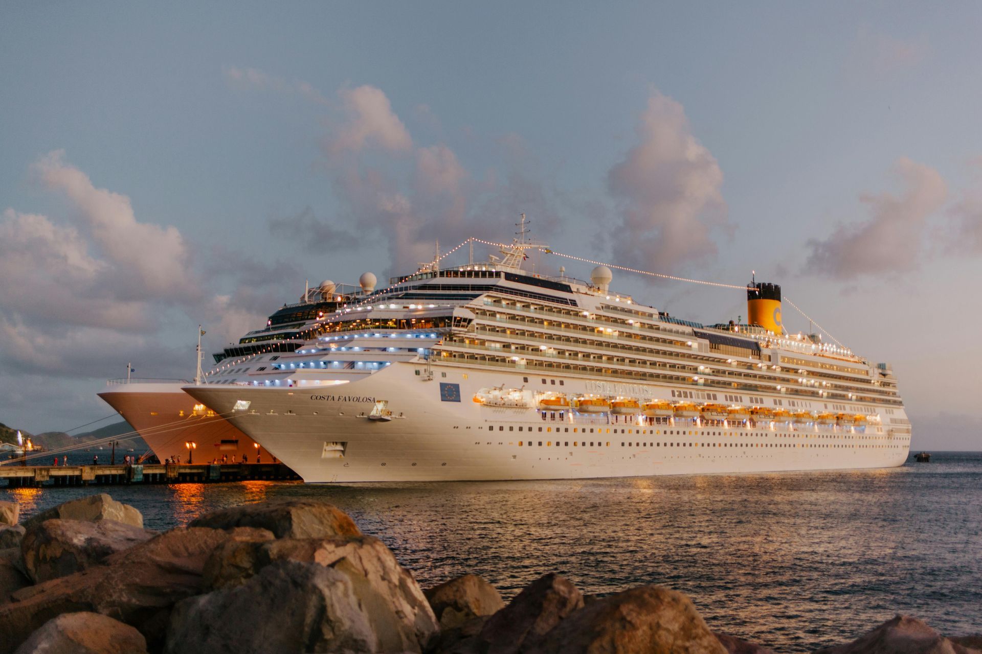 Cruise ships docked at a harbor, illuminated at dusk.