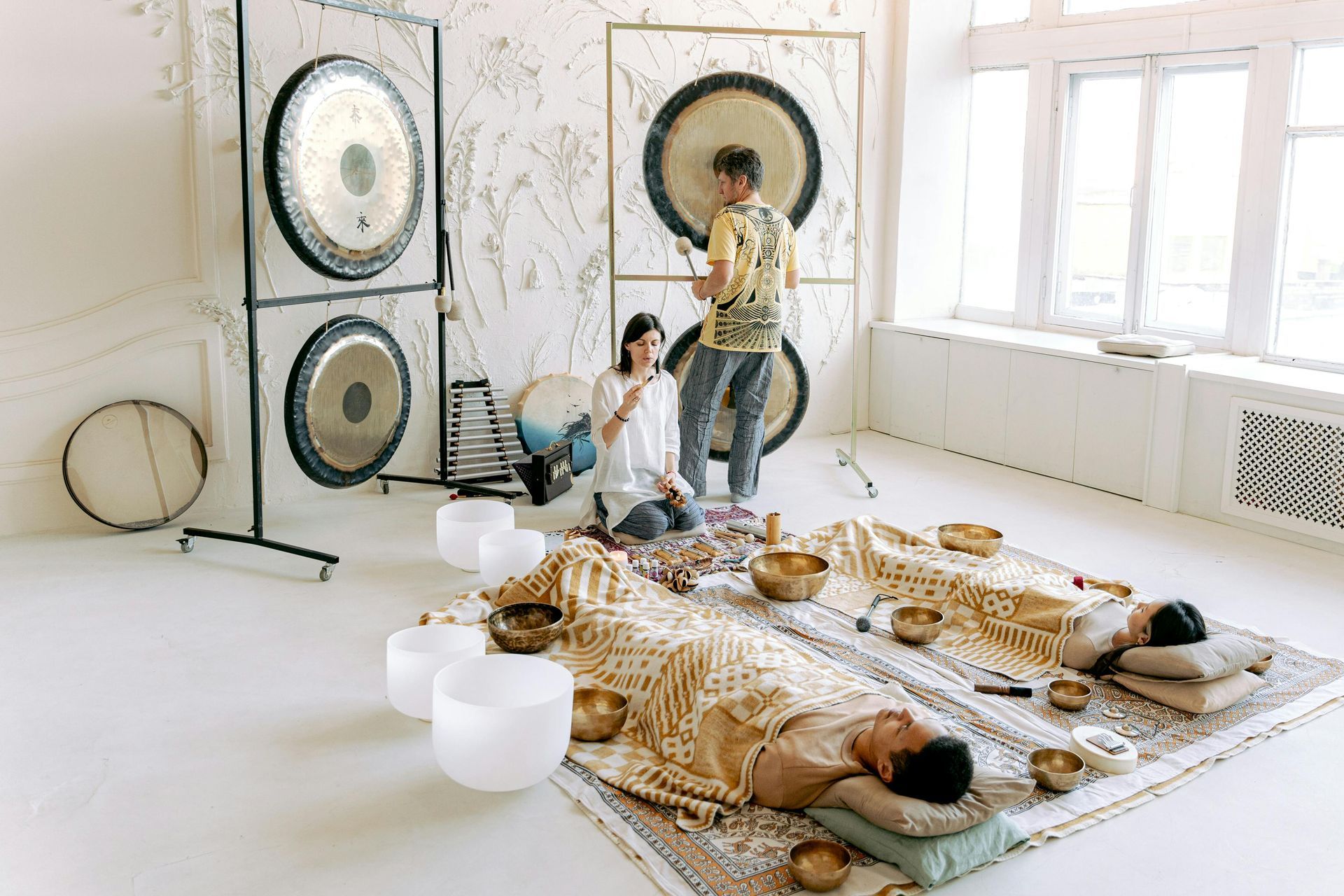 People in a sound bath room with gongs, bowls, and instruments; two people laying on mats.