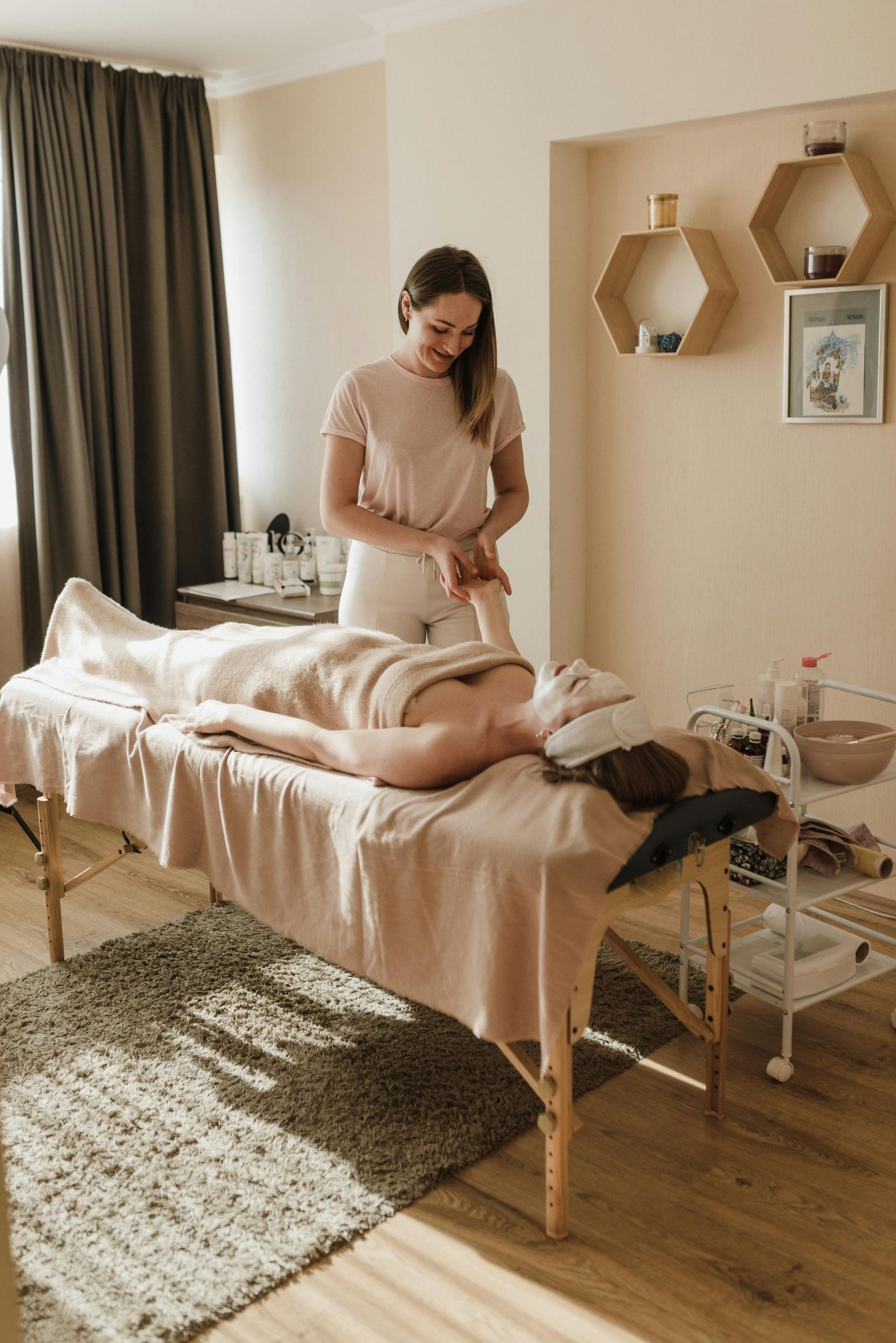 Woman receiving a massage in a spa. Therapist massages arm with light brown blanket and setting.