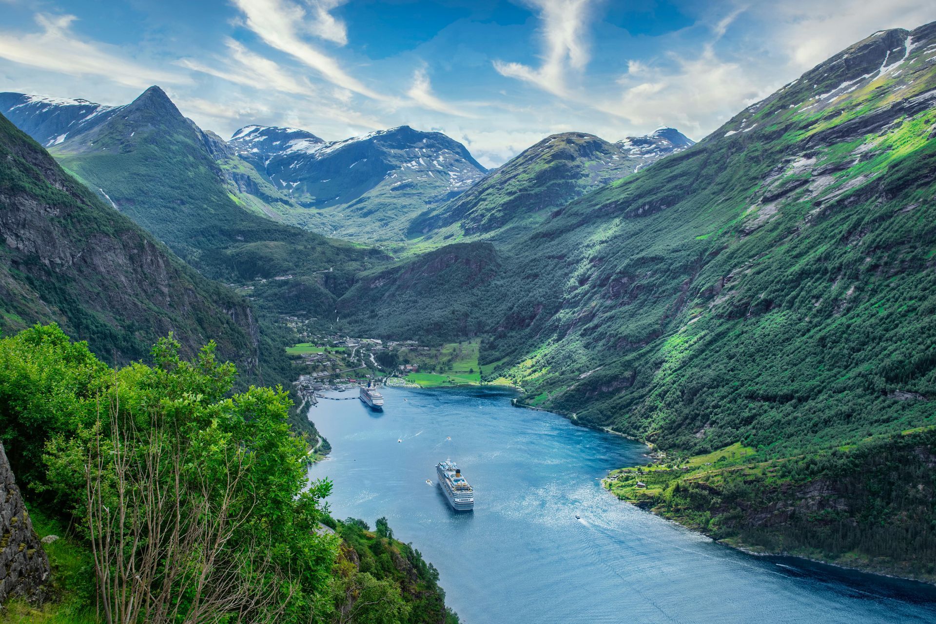 A fjord with blue water, surrounded by green mountains, featuring cruise ships.