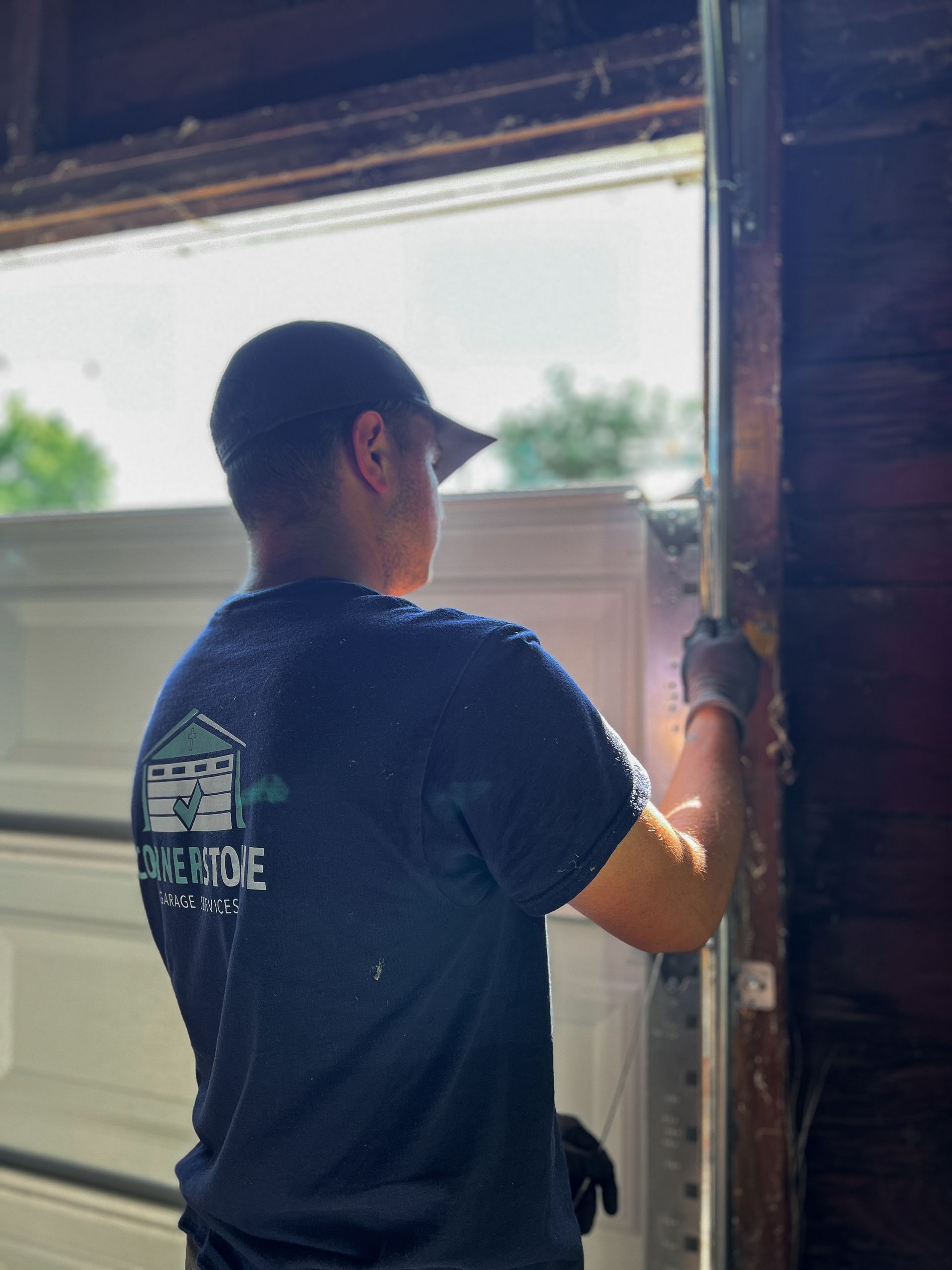 Person in blue shirt installing a garage door, sunlight streams in.